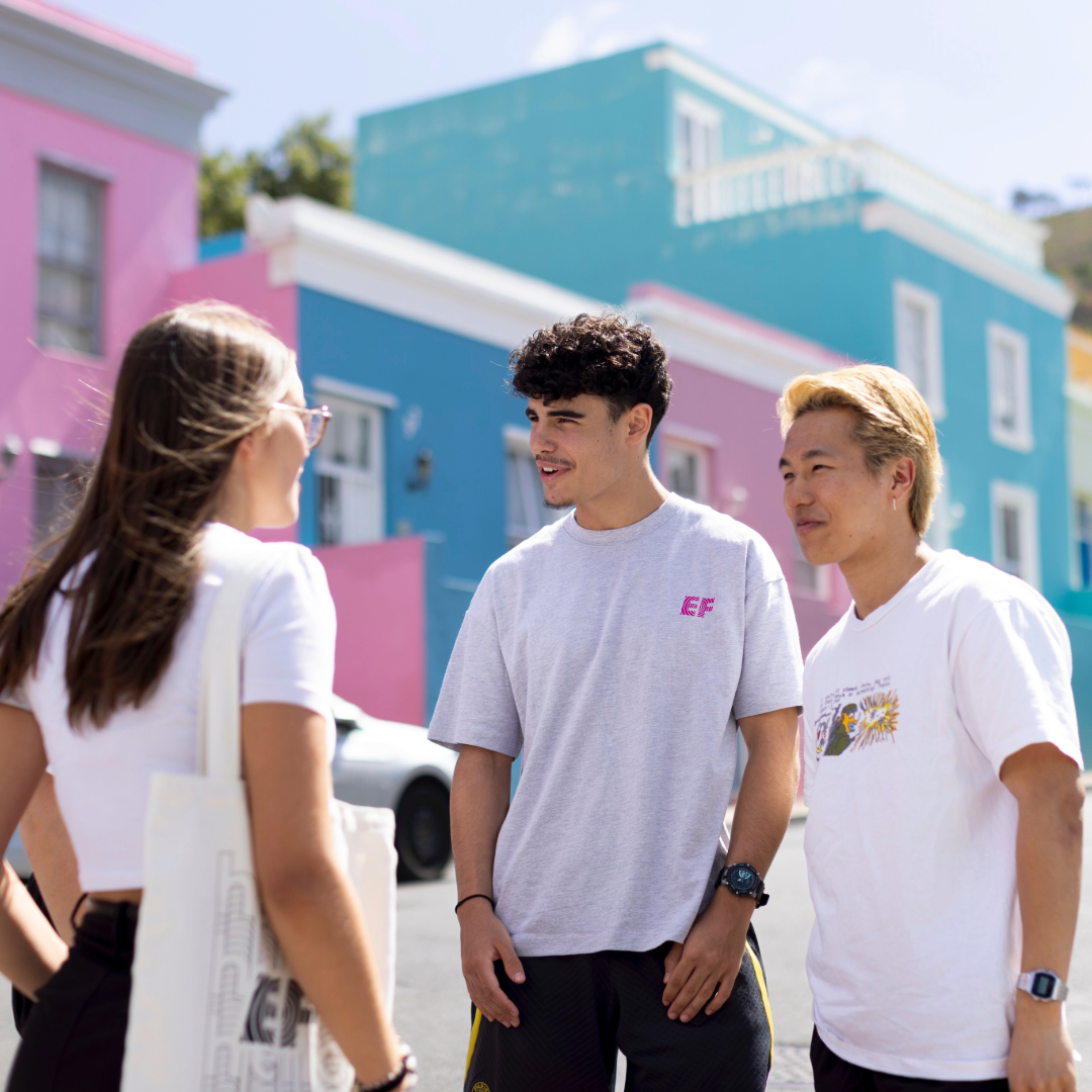Three EF Language Abroad students talking together in Cape Town’s Bo-Kaap neighborhood, standing in front of its colorful houses on a sunny day.