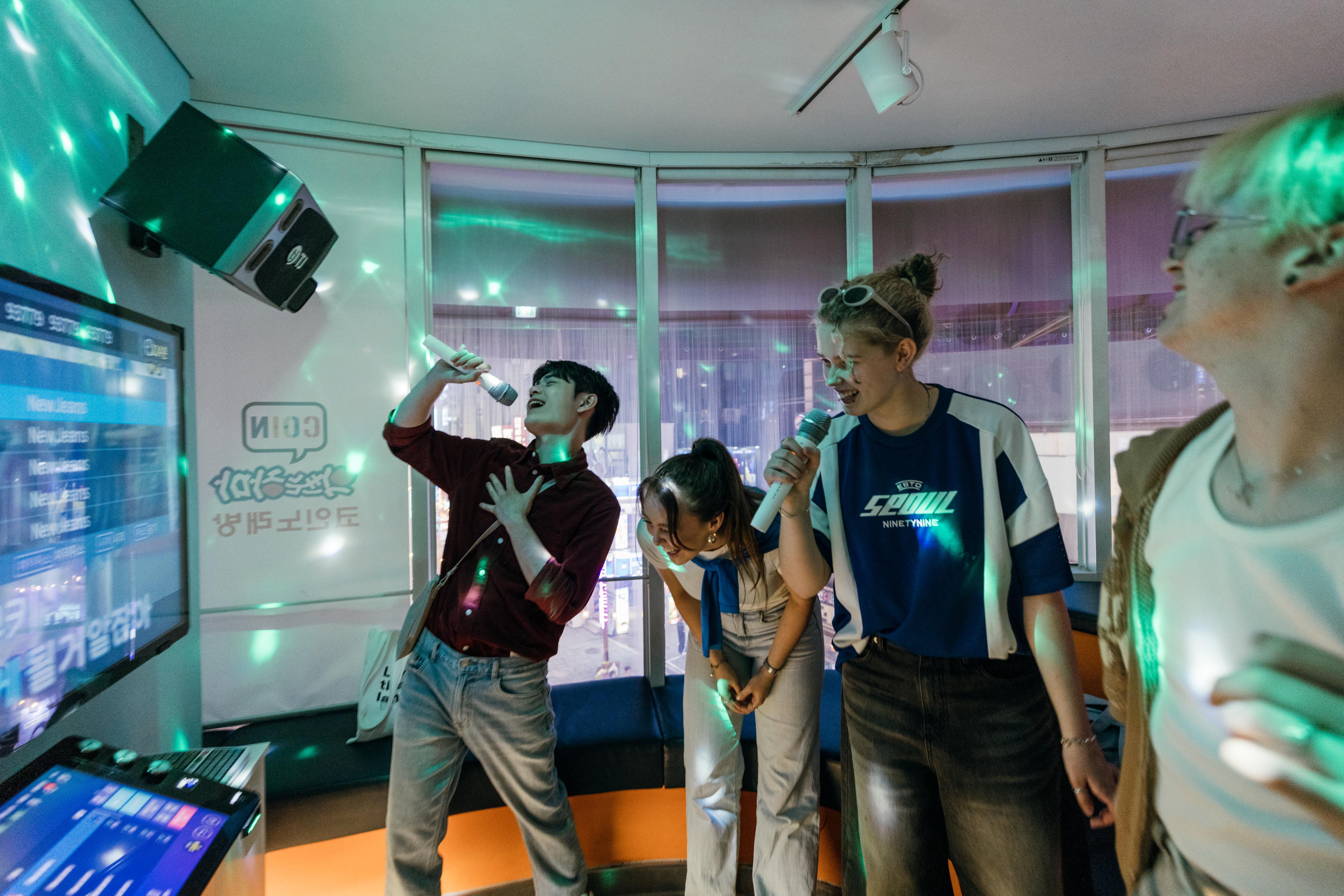 Four students enjoy a lively karaoke session, singing together and socializing in a fun, energetic atmosphere