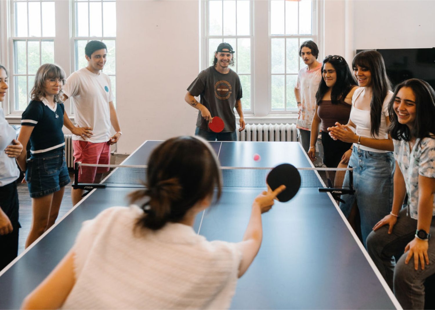 Students enjoy a friendly table tennis game while others socialize in a bright, welcoming recreation area