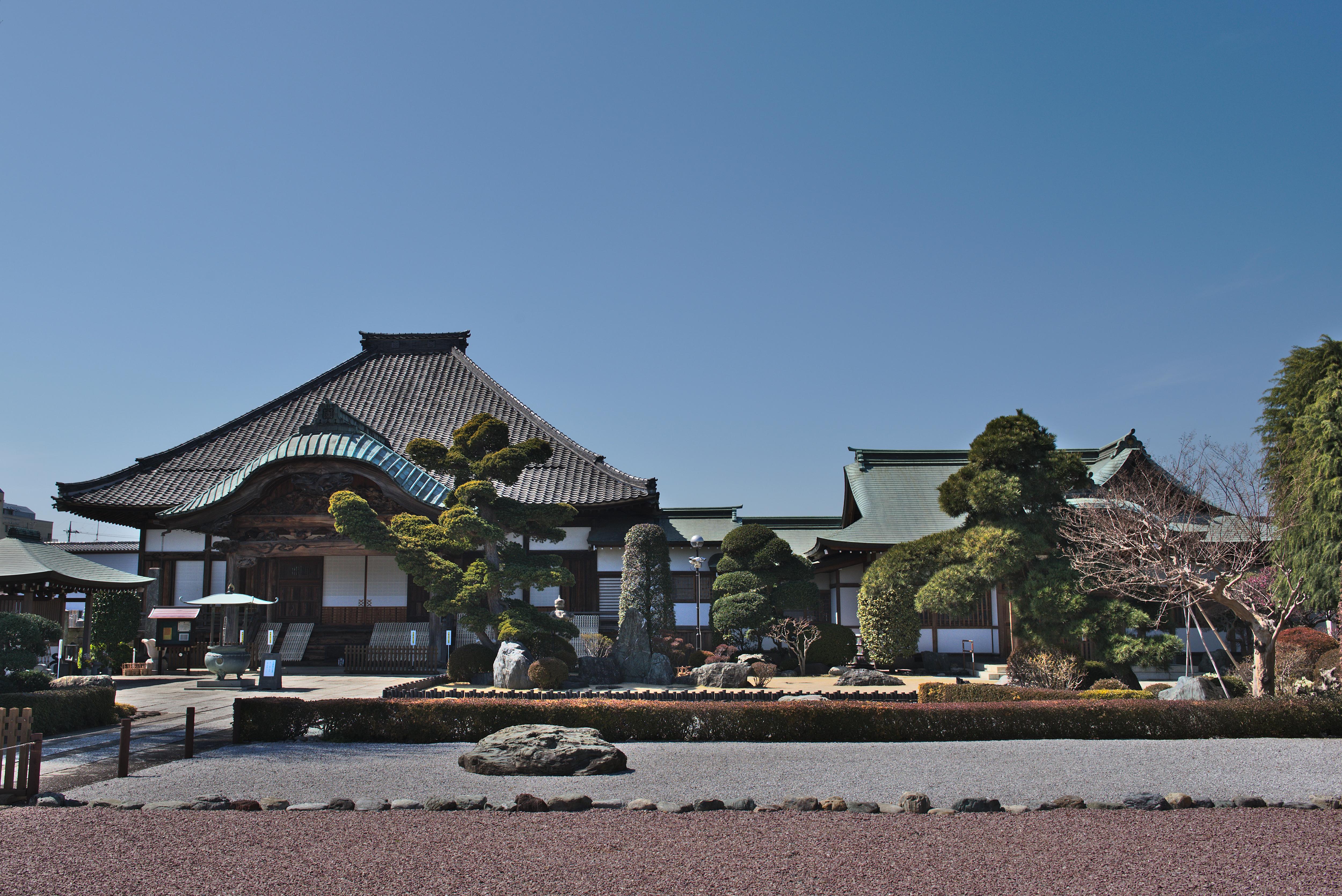 Traditional Japanese temple with curved roofs, bonsai trees, and a serene rock garden