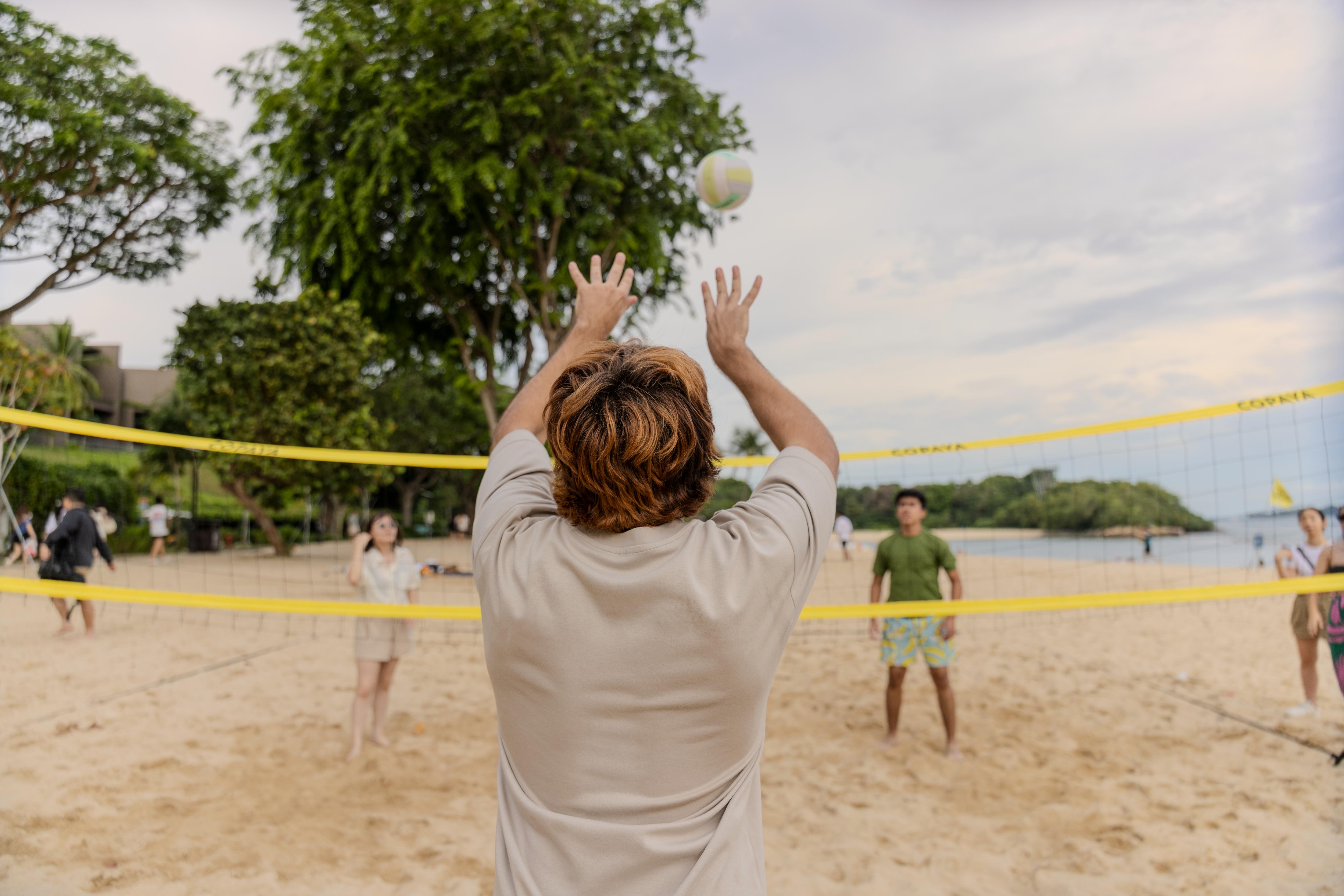 Students playing volleyball on a sandy beach court during an outdoor game