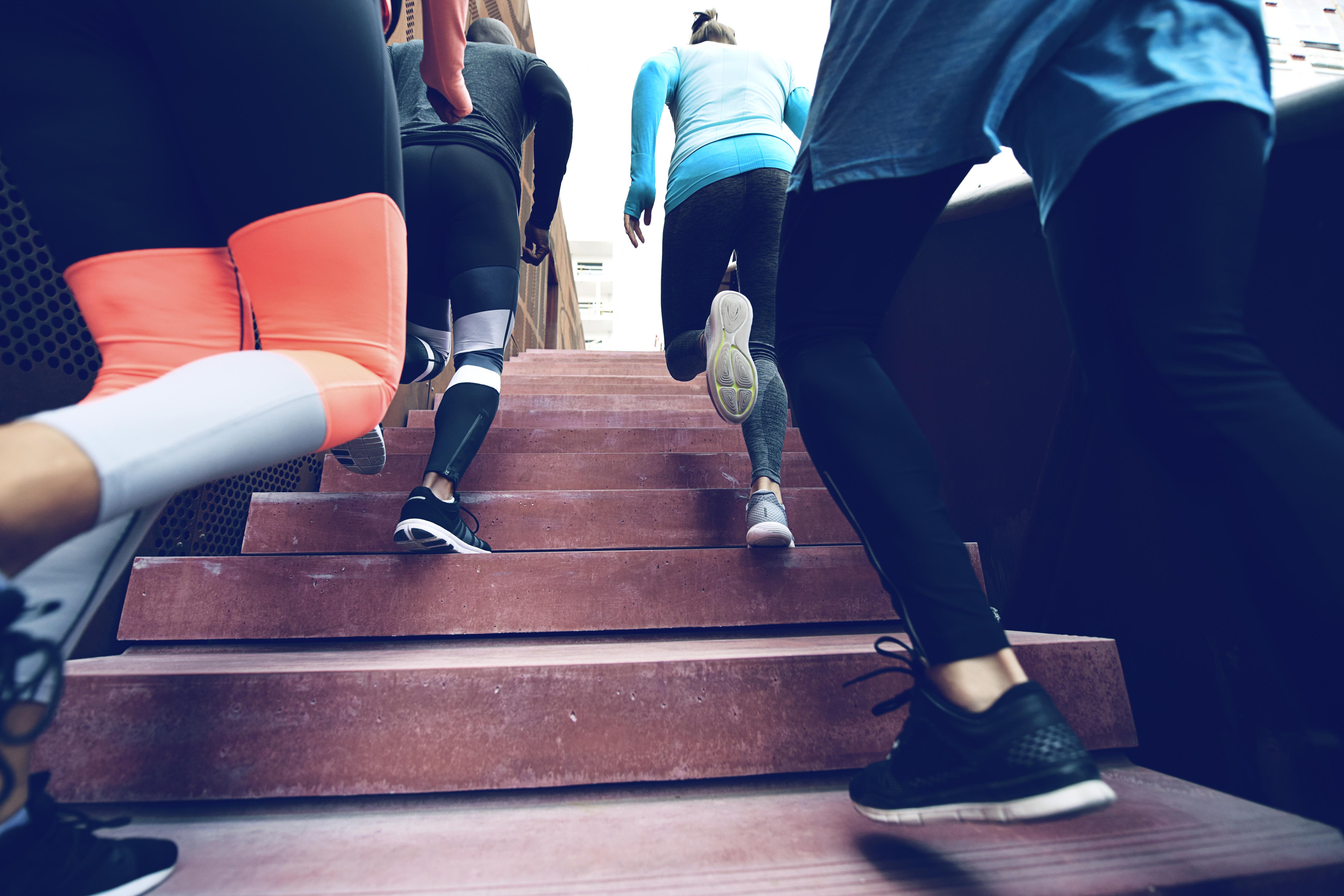 Four students exercise together, running up outdoor stairs during an energetic fitness activity