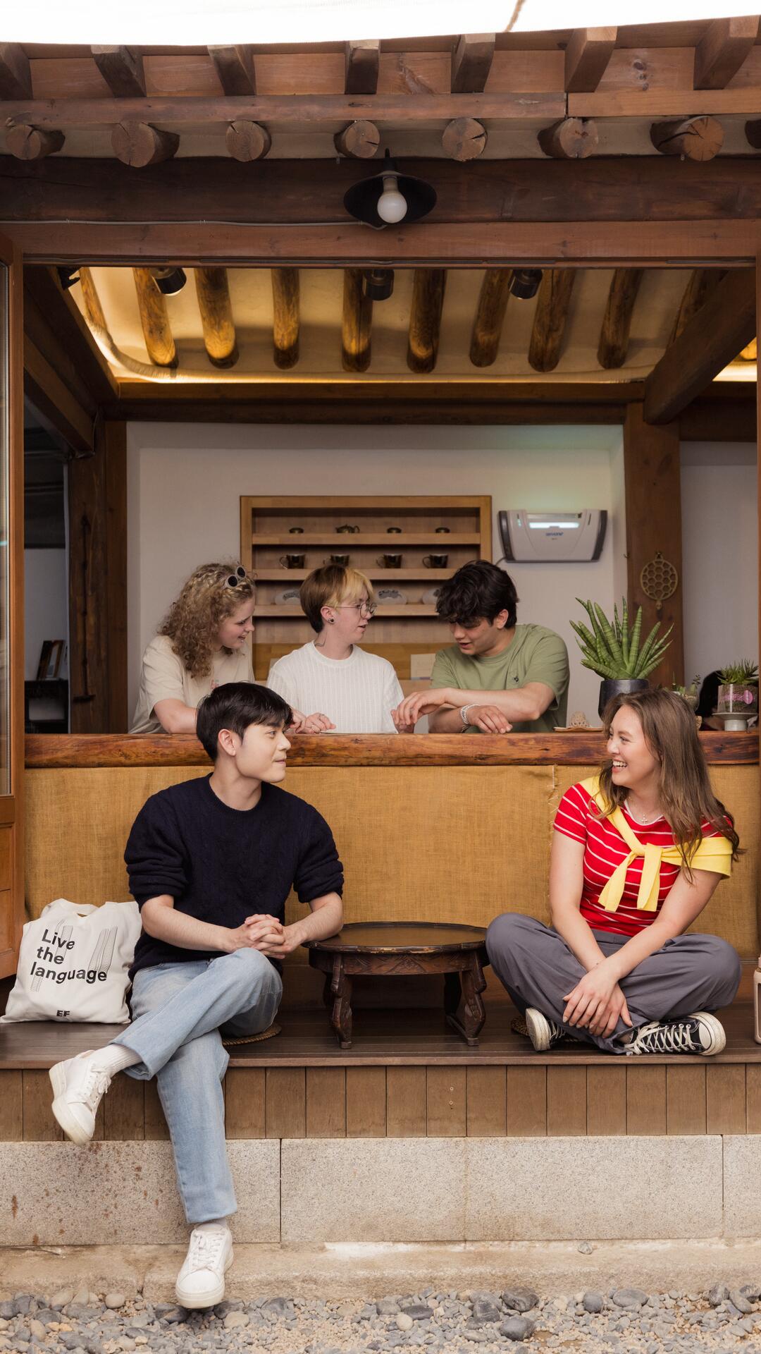 EF Language Abroad students hanging out together at a traditional tea house in Seoul, sharing snacks and talking while sitting by the wooden counter and open doorway.
