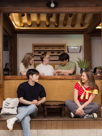 EF Language Abroad students hanging out together at a traditional tea house in Seoul, sharing snacks and talking while sitting by the wooden counter and open doorway.