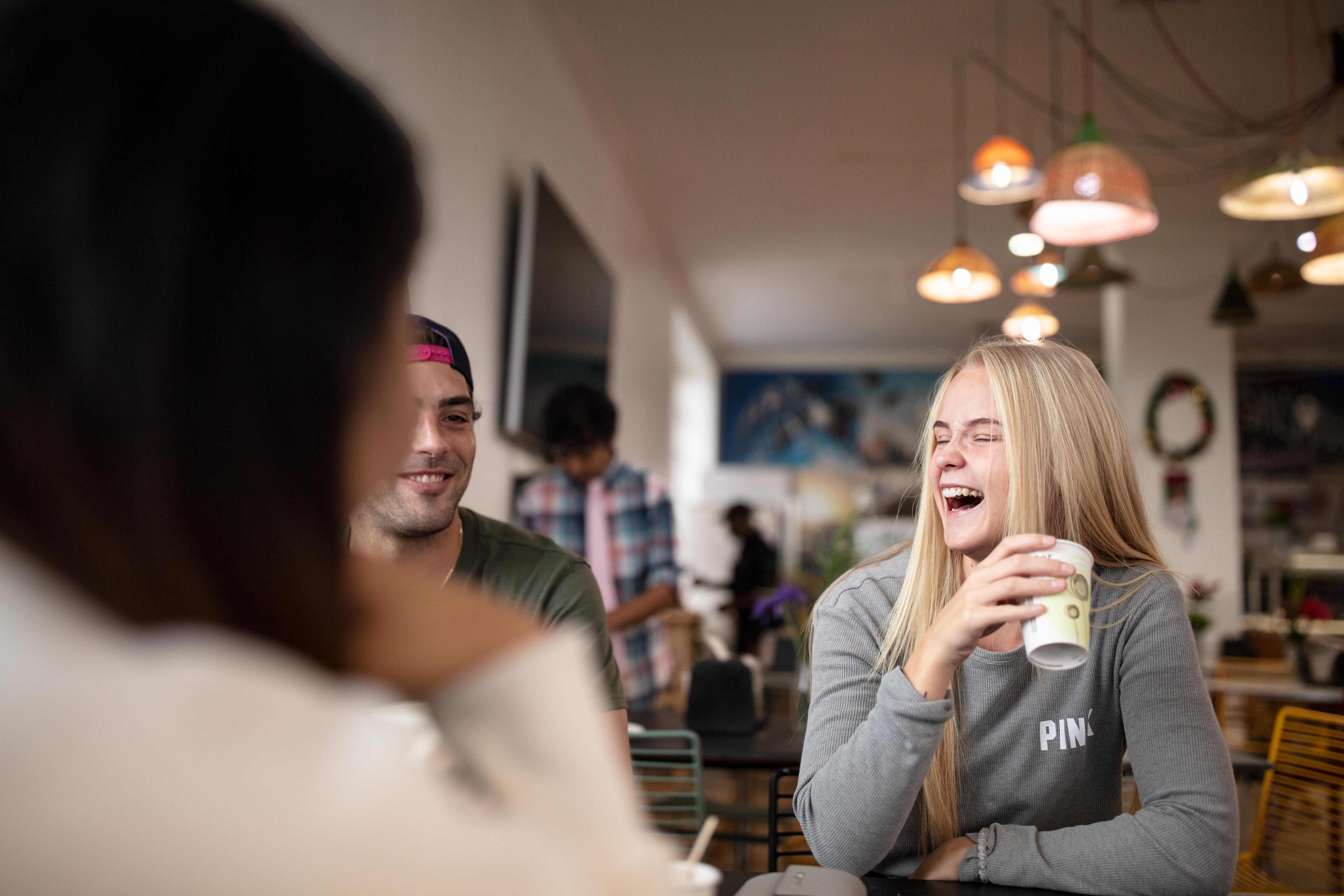 Three students enjoy coffee and conversation in a cafe socializing