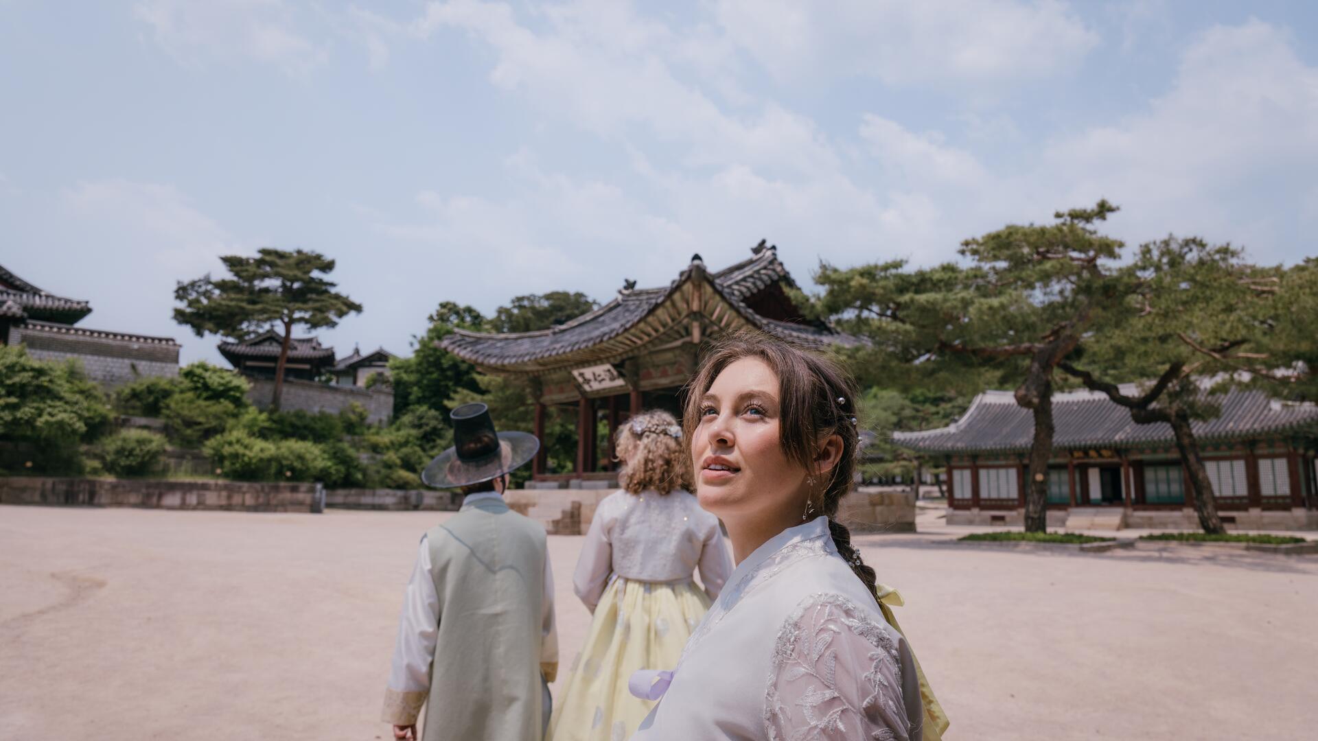 EF Language Abroad students exploring a traditional palace in Seoul, wearing hanbok and walking through historic courtyards surrounded by ornate wooden buildings and pine trees.