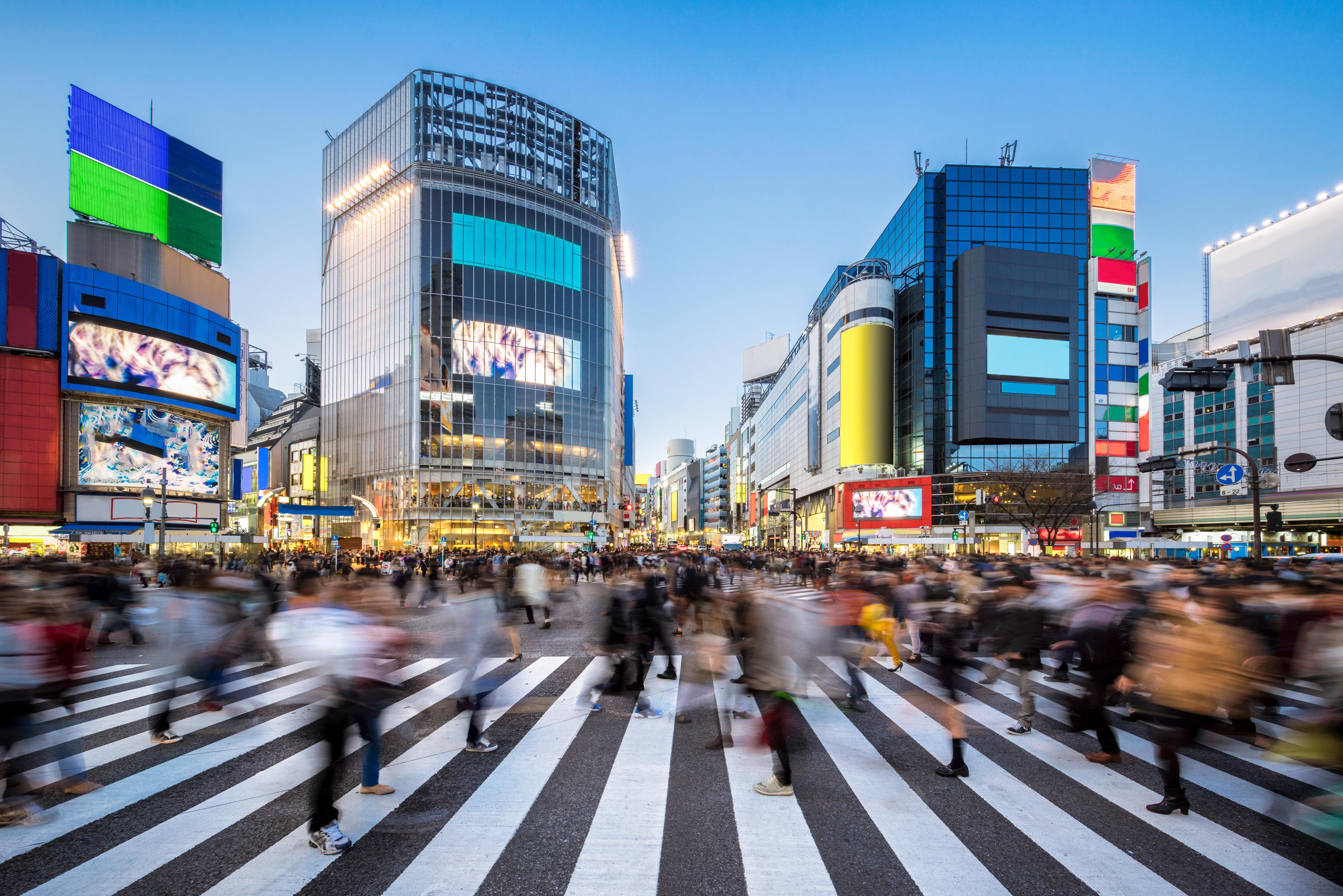 Shibuya Crossing at night, bustling with pedestrians and illuminated by vibrant city billboards
