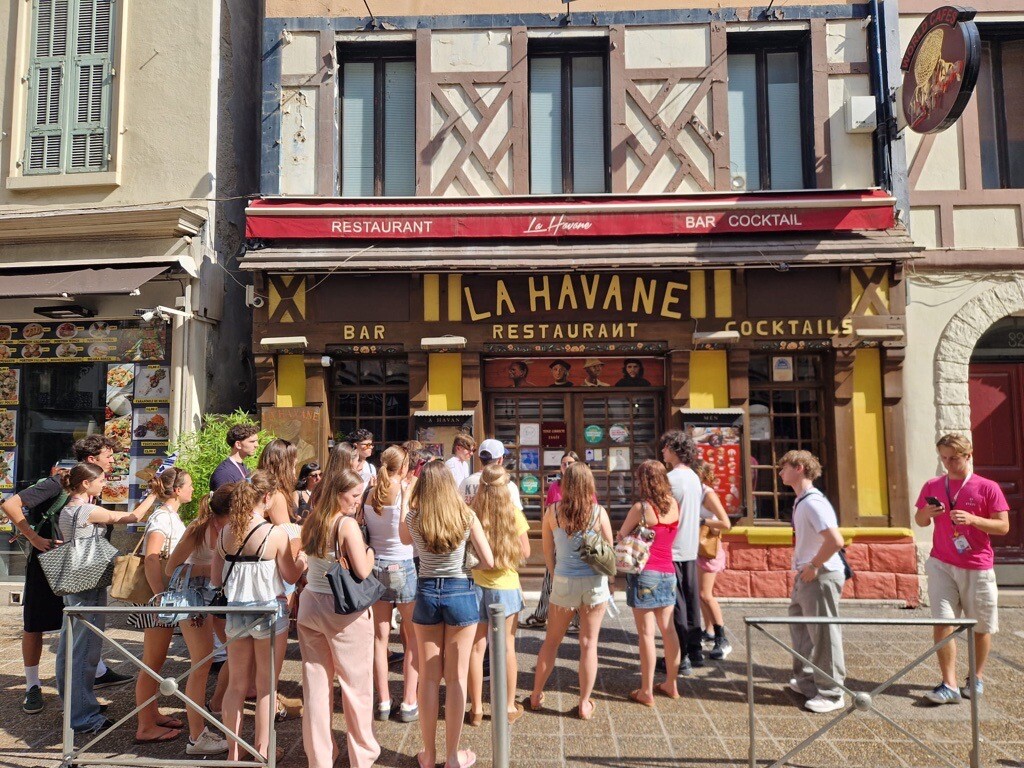 Students gather outside a local restaurant, socializing and enjoying a shared dining experience in a vibrant community setting