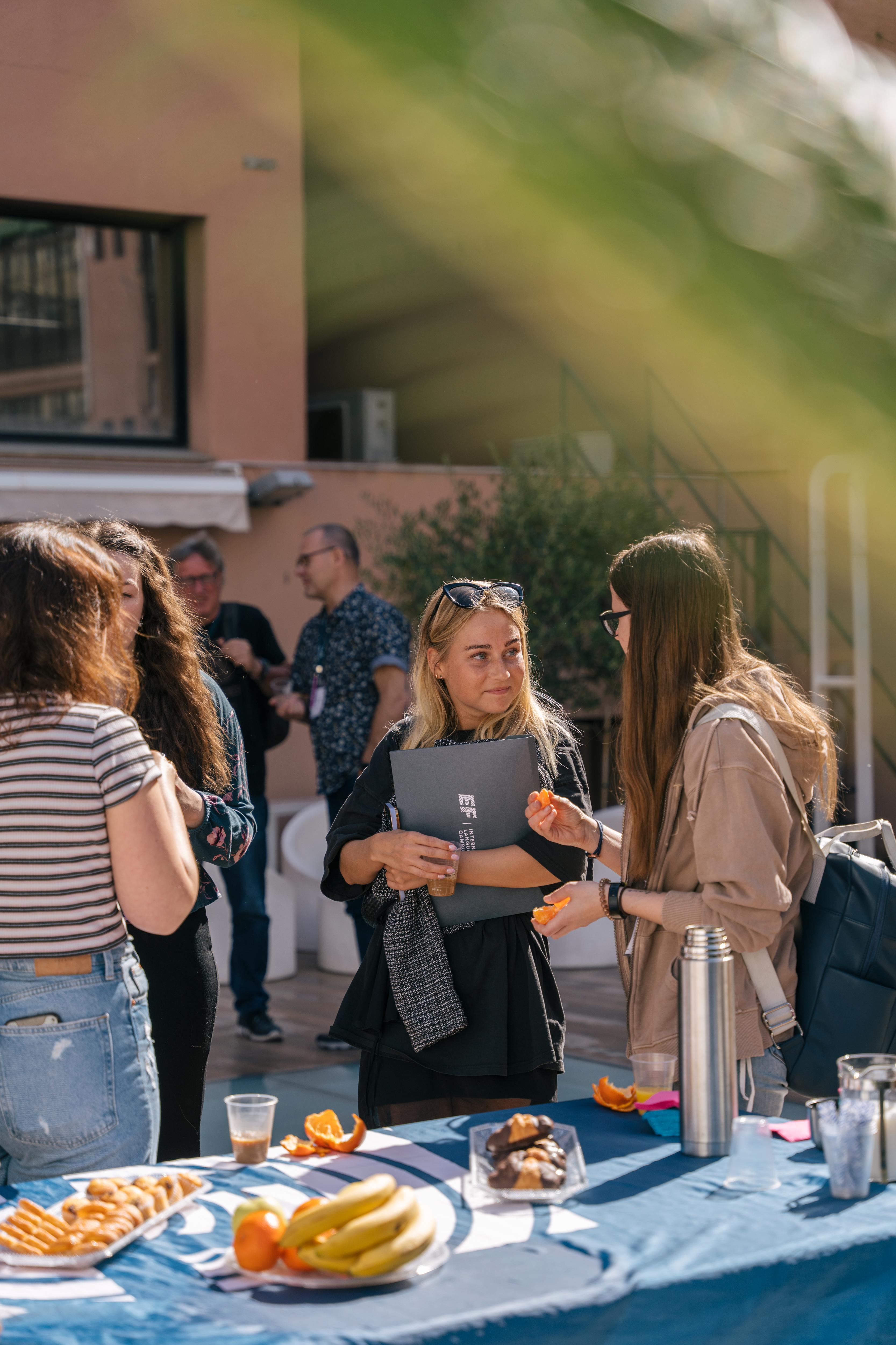 Students socialize and enjoy refreshments on a terrace, connecting in a relaxed and welcoming outdoor setting
