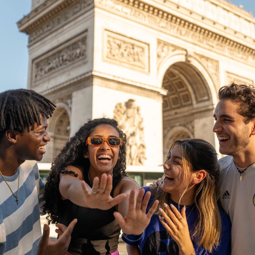Four EF Language Abroad students laughing together in front of the Arc de Triomphe in Paris while exploring the city on a sunny day.