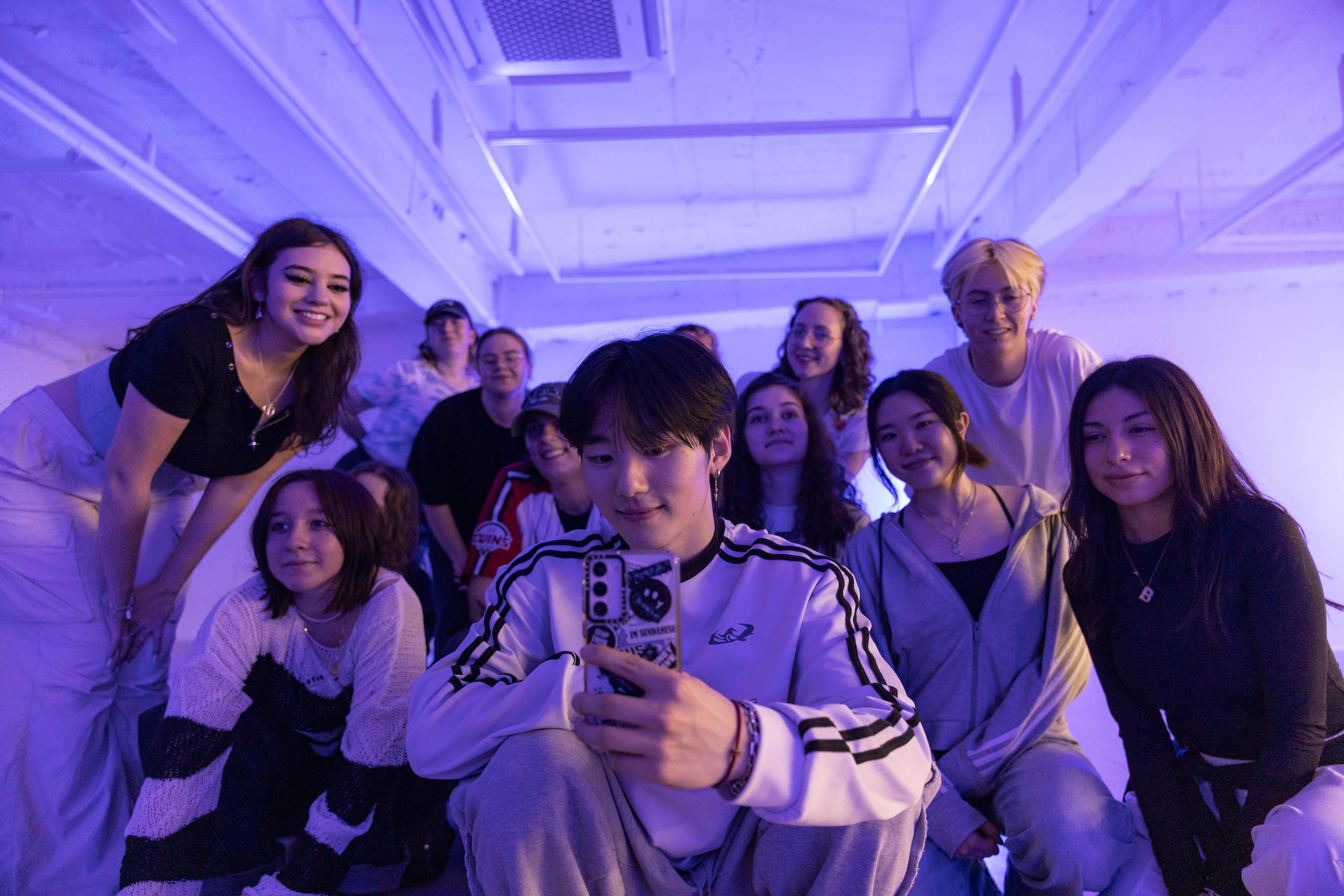 Students performing a K-pop dance challenge together under vibrant purple lighting