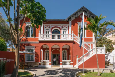 EF Language Abroad students walking and gathering outside a historic red campus building in Málaga, Spain, surrounded by palm trees and outdoor seating areas.