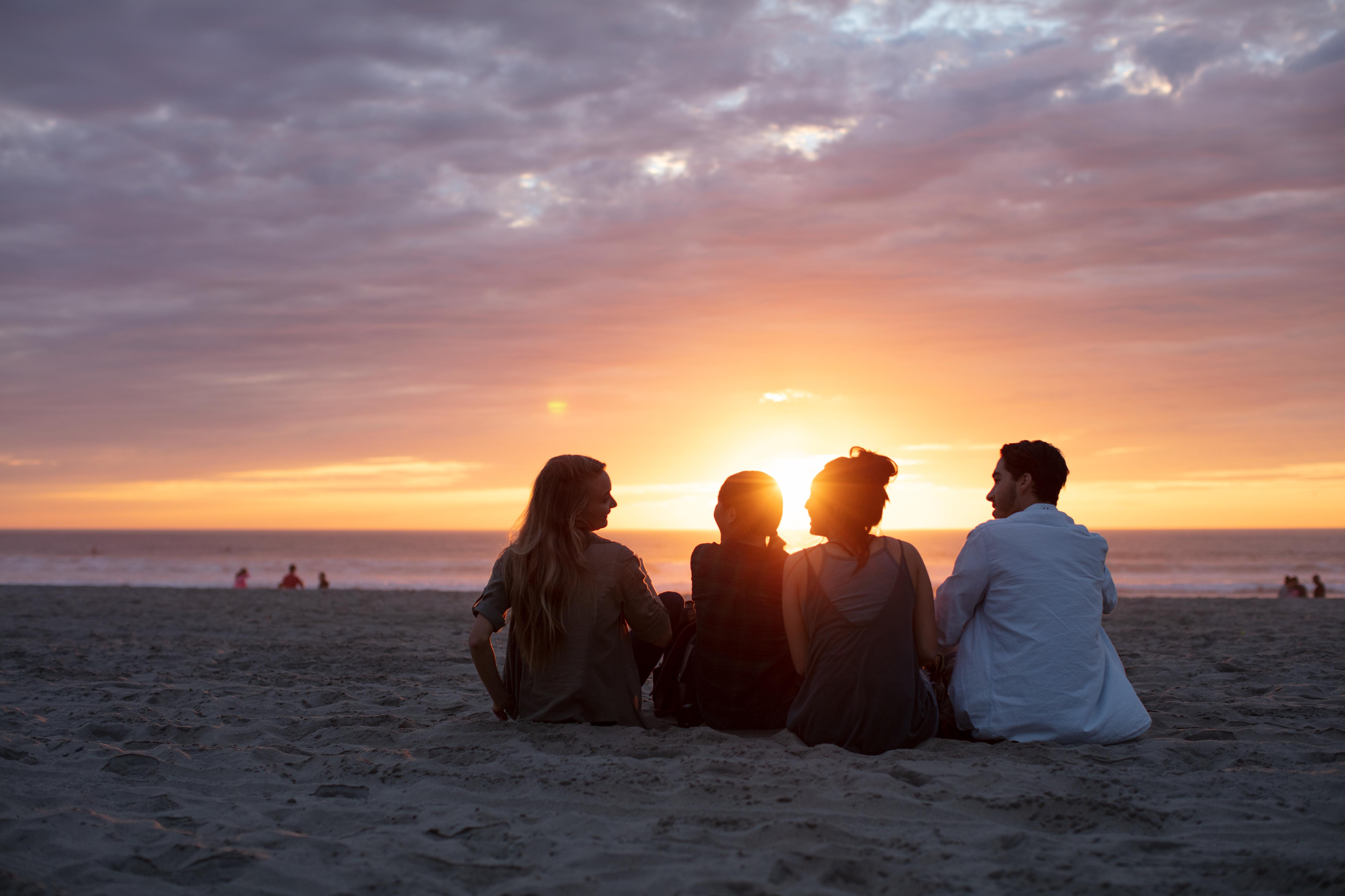 Students relax on a beach at sunset, enjoying ocean views and a peaceful shared experience