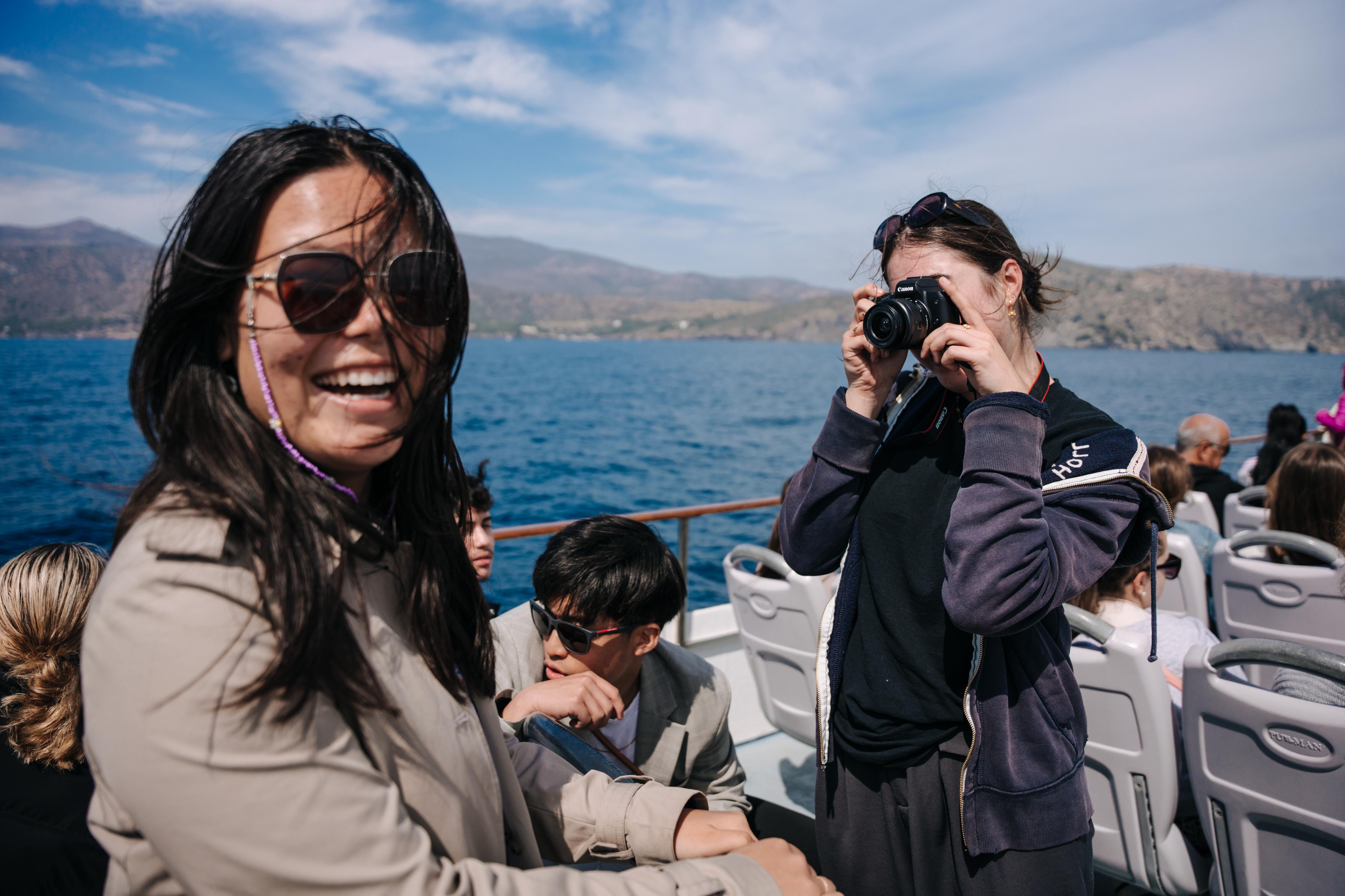 Students enjoy a scenic boat trip, socializing and capturing memorable moments against a beautiful coastal backdrop