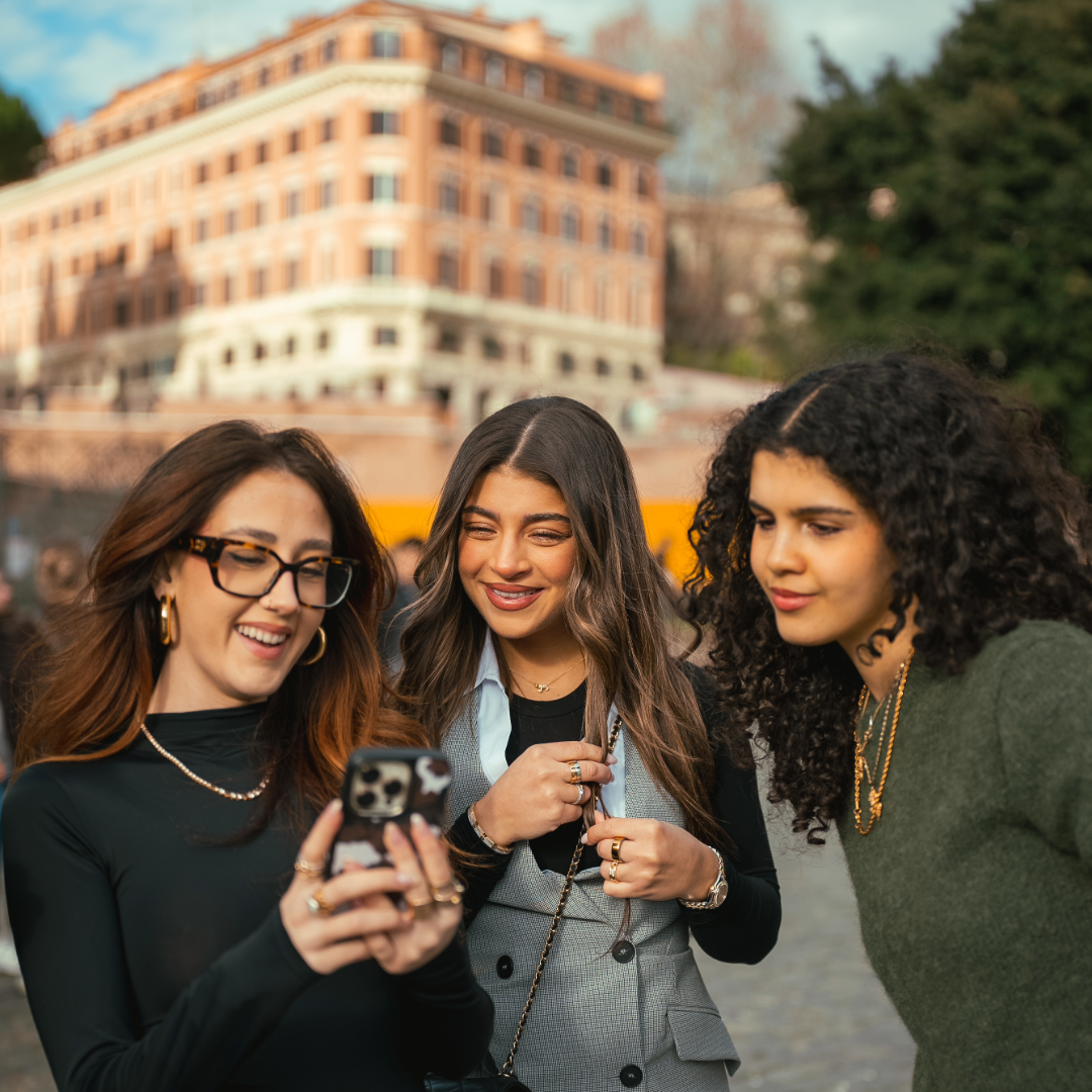 Three EF Language Abroad students in Rome smiling and looking at a phone together while exploring the city on a sunny day.