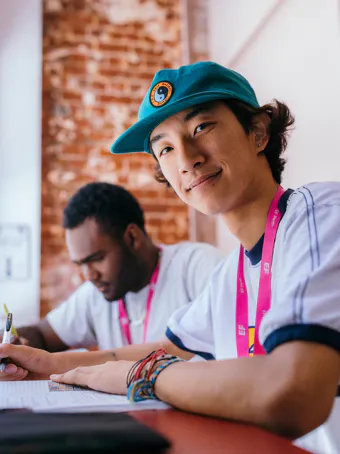 EF Language Abroad students studying together in a classroom, with one student smiling toward the camera while working on an assignment at their desk.