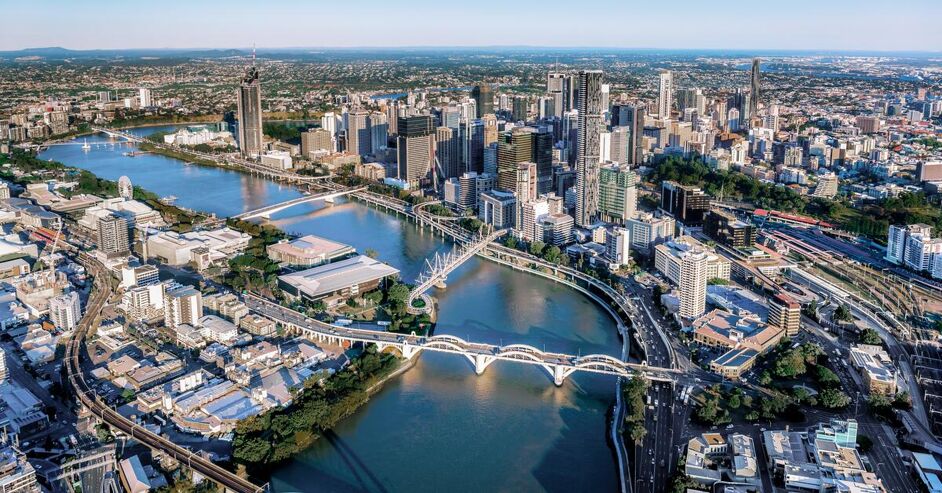 This is a wide aerial view of a bustling city with a river winding through it, crossed by multiple bridges. Tall buildings line the riverbanks, creating an impressive skyline.