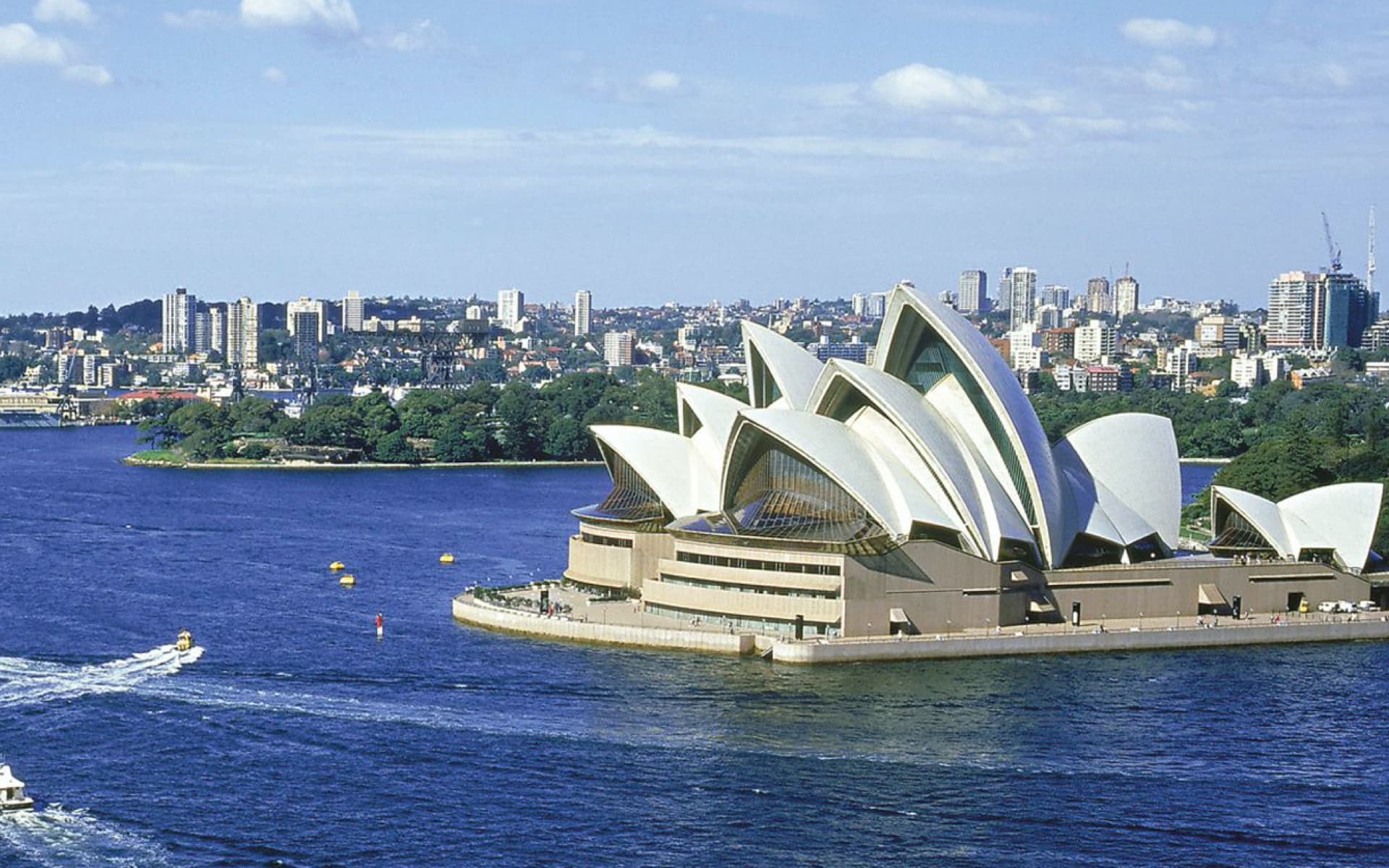 The image displays the iconic Sydney Opera House, a famous Australian landmark, with the city skyline in the background and boats on the water.