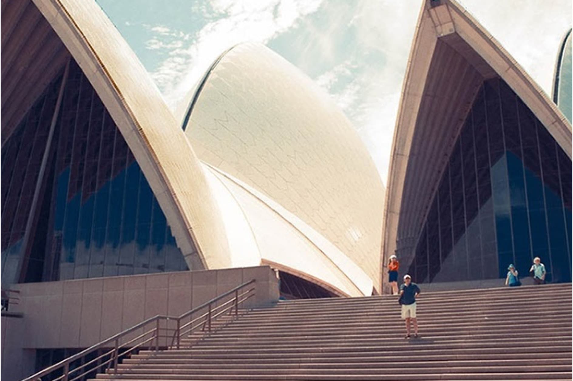 The image showcases the Sydney Opera House, an iconic Australian landmark, featuring its distinctive sail-like architecture and a grand staircase leading to its entrances.