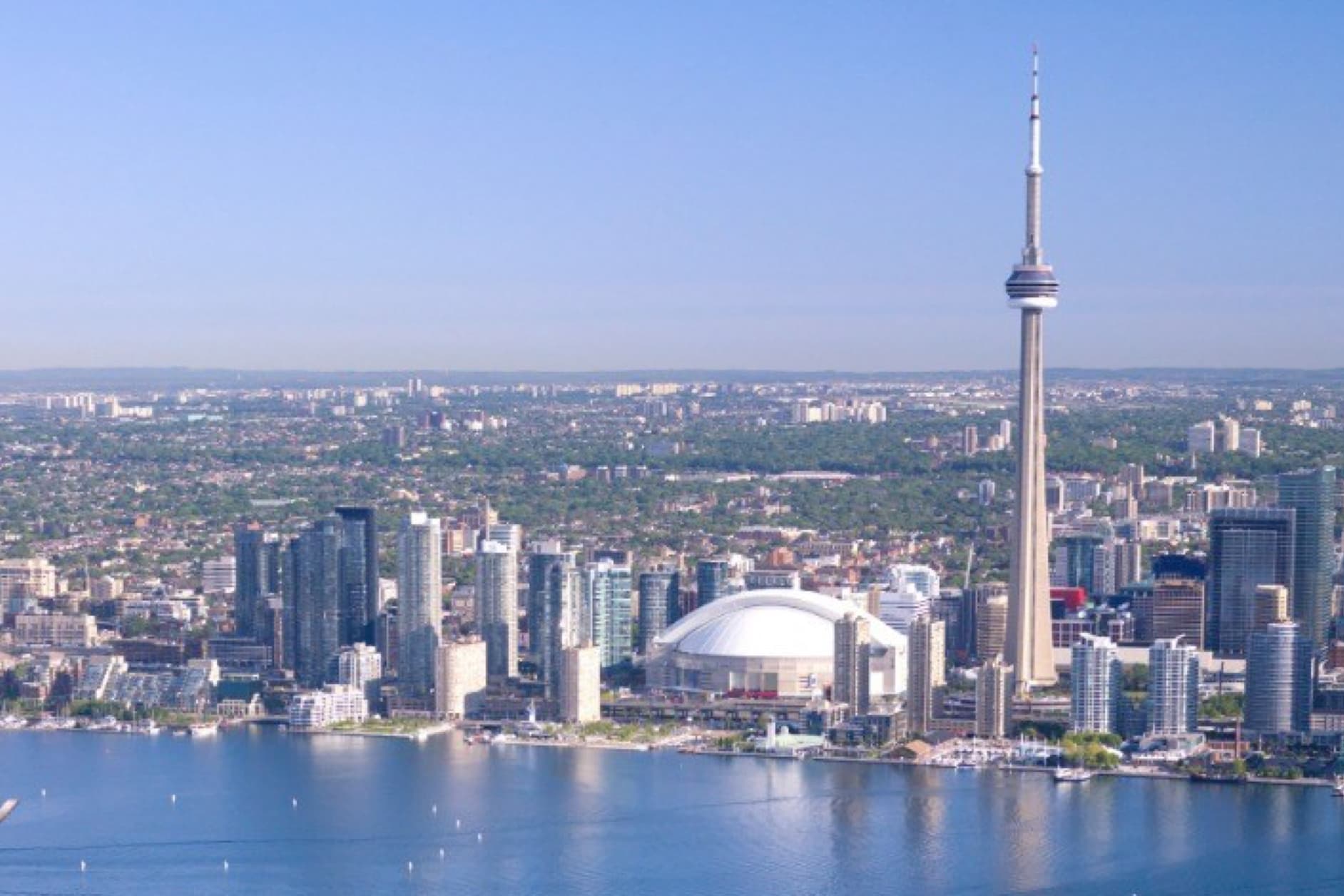 An impressive aerial view of the Toronto, Canada skyline, featuring the CN Tower and Rogers Centre rising above Lake Ontario.