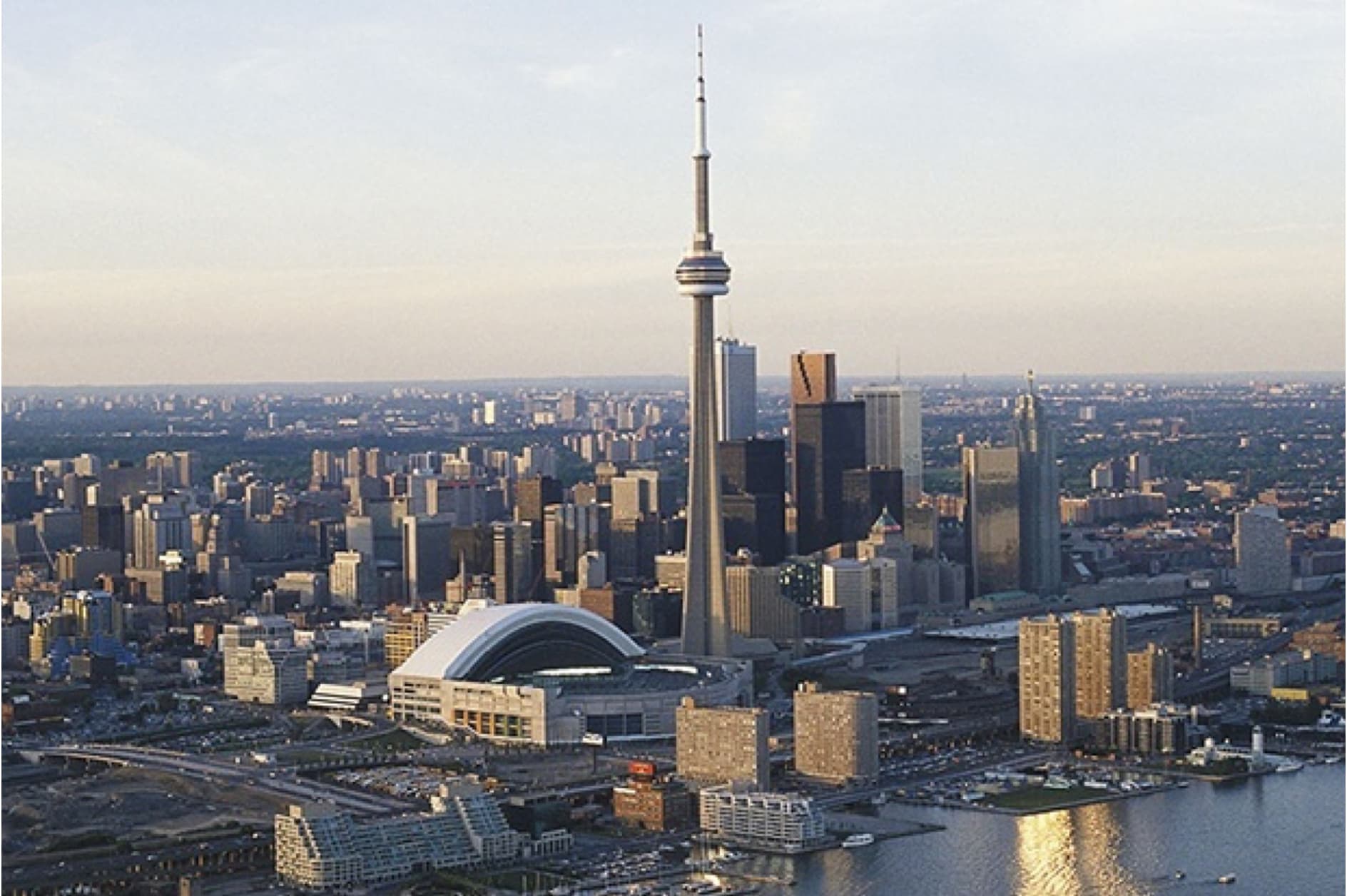 This image showcases a stunning aerial view of the Toronto skyline in Canada, prominently featuring the iconic CN Tower, surrounded by numerous skyscrapers and the Rogers Centre.