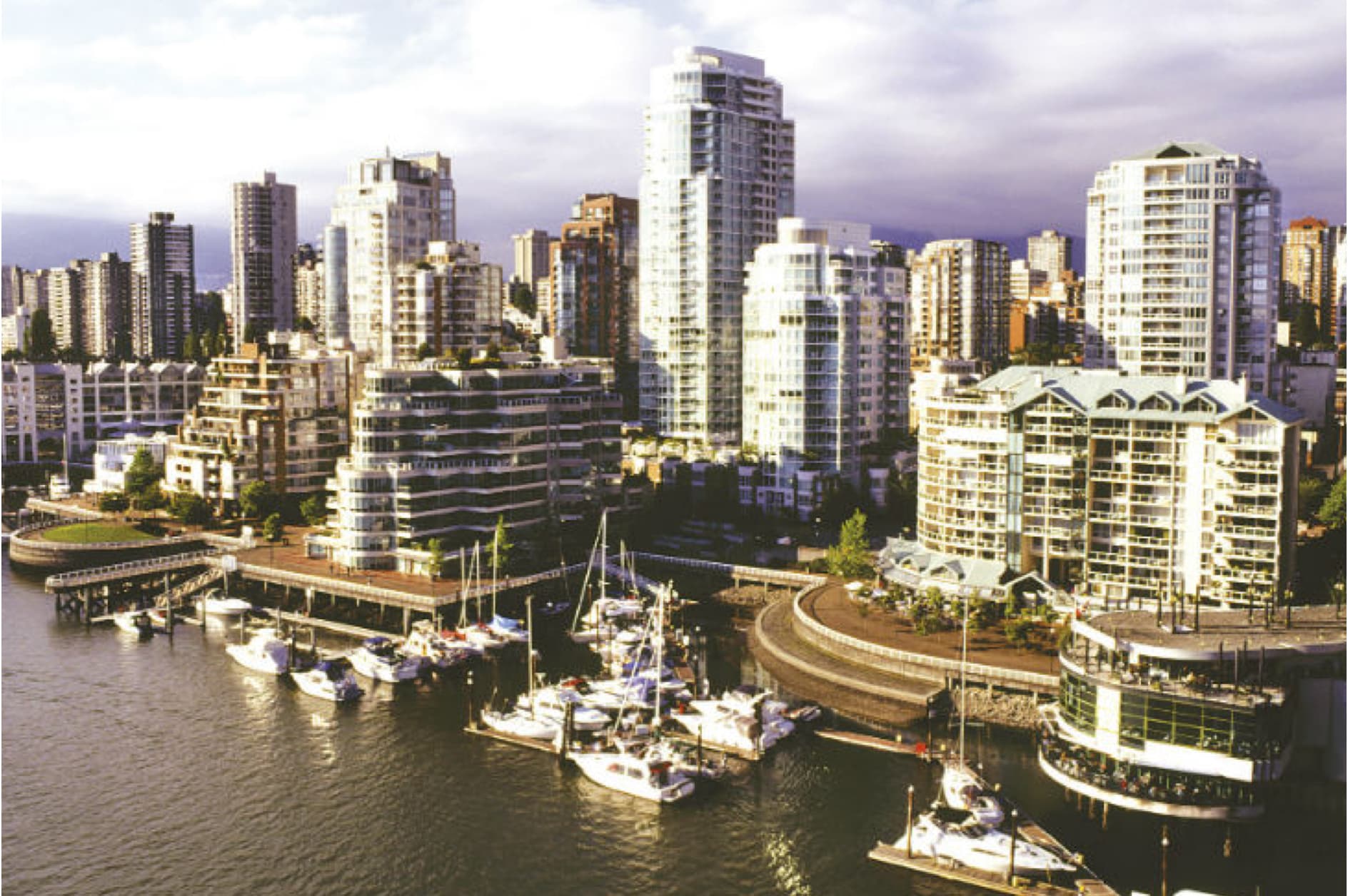 A picturesque view of a bustling waterfront city, featuring modern high-rise buildings and a marina filled with sailboats.