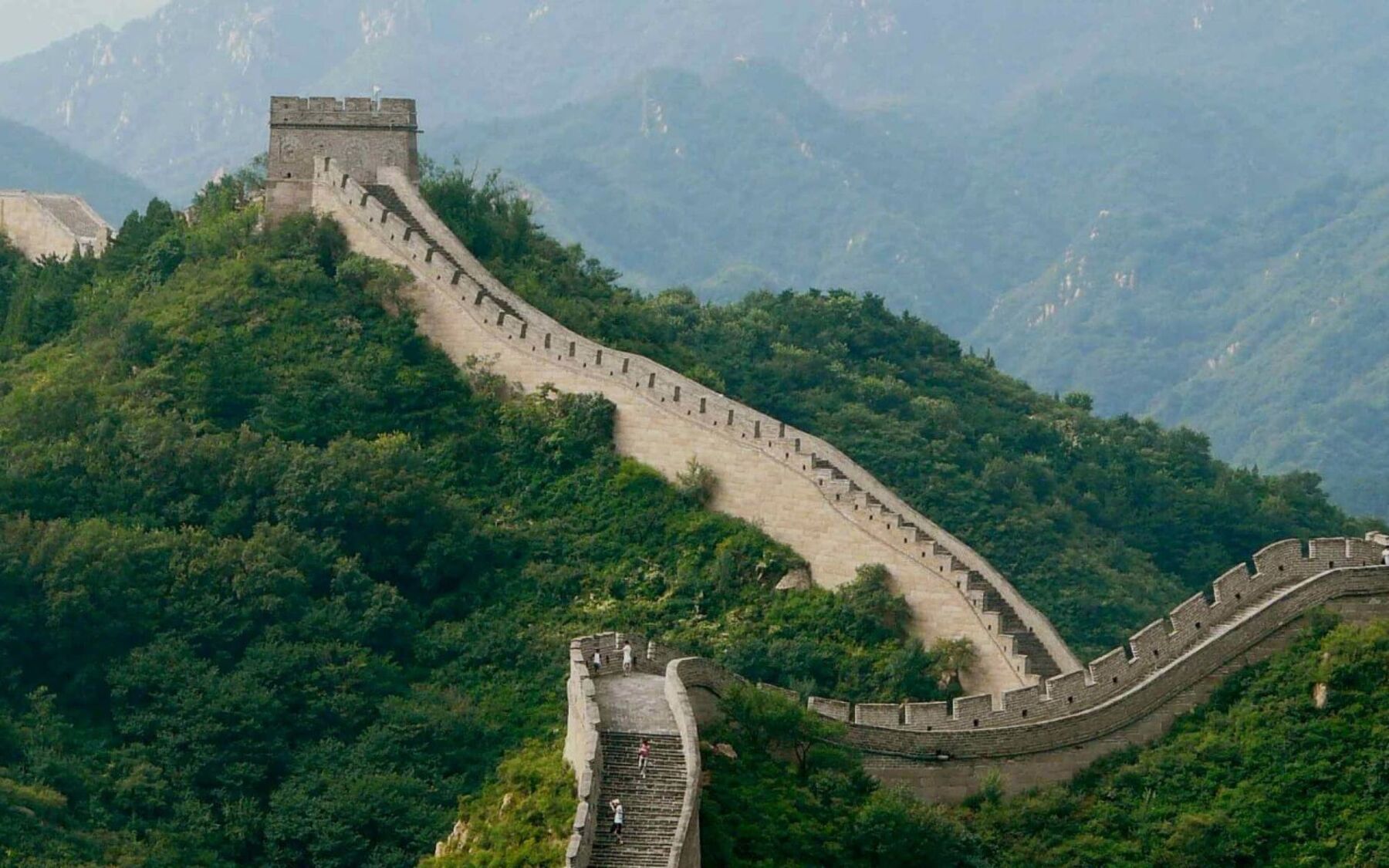 The Great Wall of China snakes across verdant mountains, an impressive testament to ancient engineering and history stretching into the distance.