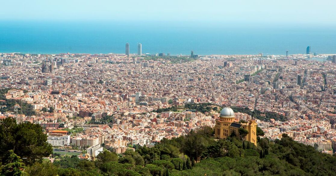 A wide shot of Barcelona overlooking the city and the sea in the background. An observatory is visible on a hill in the foreground.