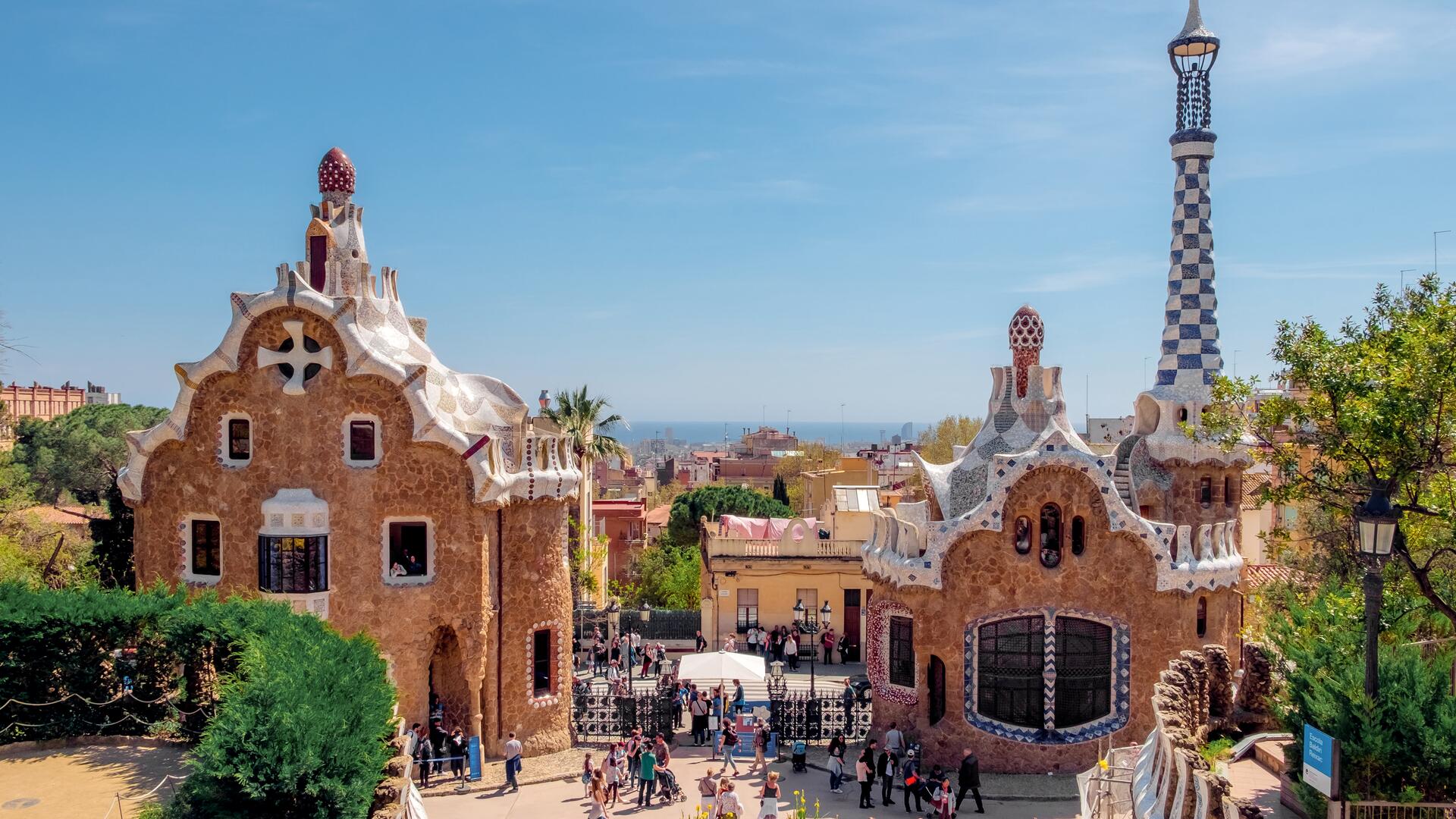 This is an image of Park Güell in Barcelona, Spain, designed by Antoni Gaudí. It features unique architecture with colorful mosaics and whimsical structures, set against a clear blue sky.
