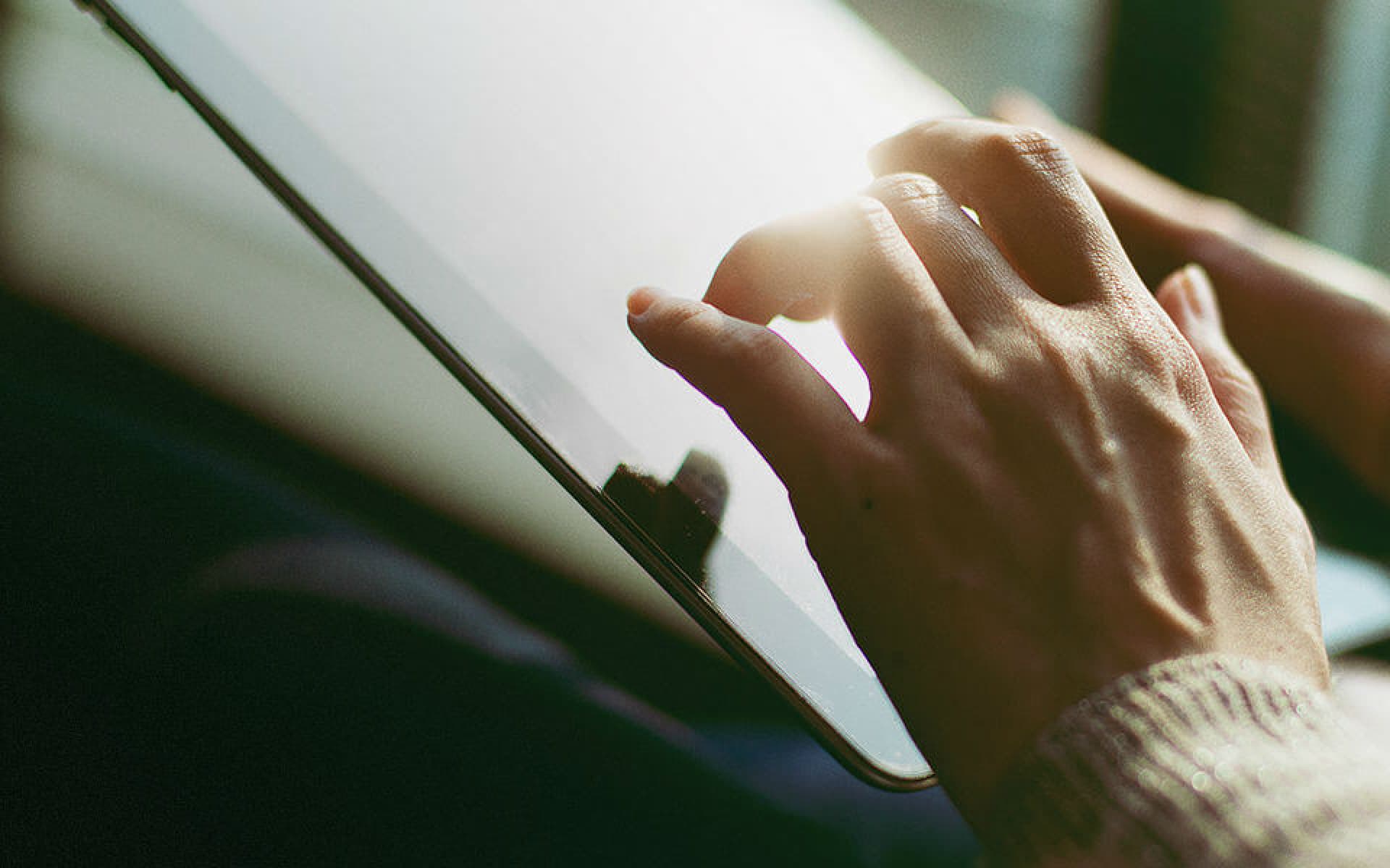 The image shows a close-up of a person's hands using a tablet device. The fingers are actively interacting with the screen, suggesting engagement with digital content or an application.