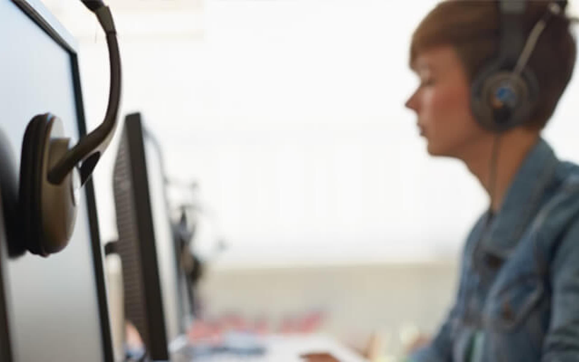 A young woman wearing headphones is seated in front of a computer monitor, typing on a keyboard, suggesting a learning or work environment.