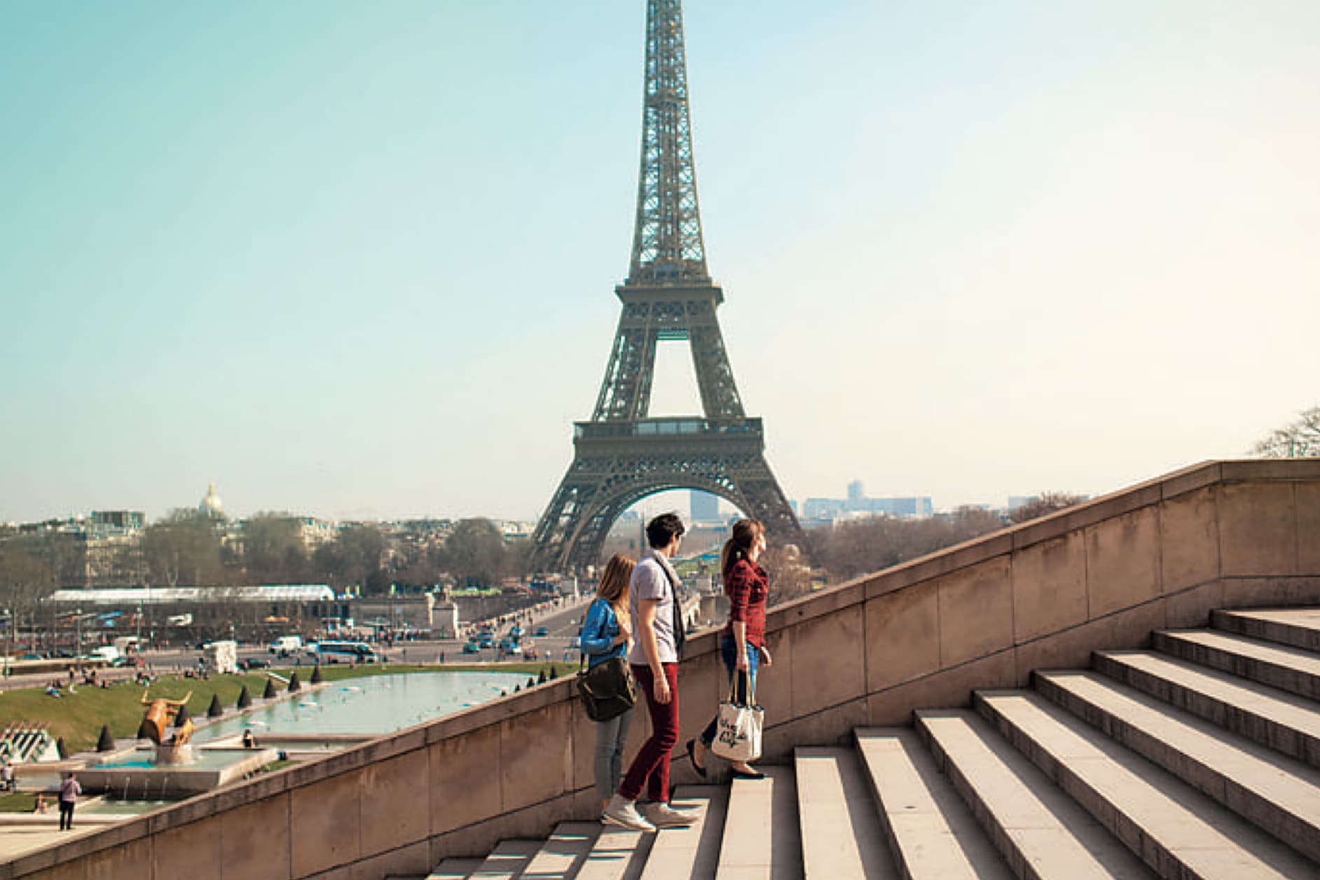 Several people ascend a staircase, with the Eiffel Tower visible in the background on a sunny day.