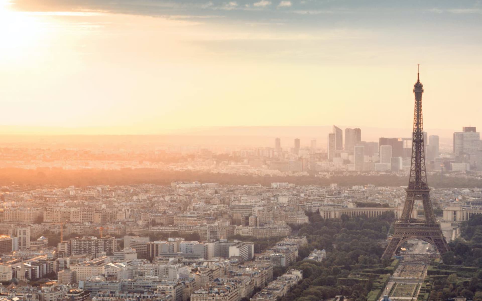 A picturesque view of Paris at sunset, with the Eiffel Tower prominent in the foreground and the city skyline stretching into the distance.