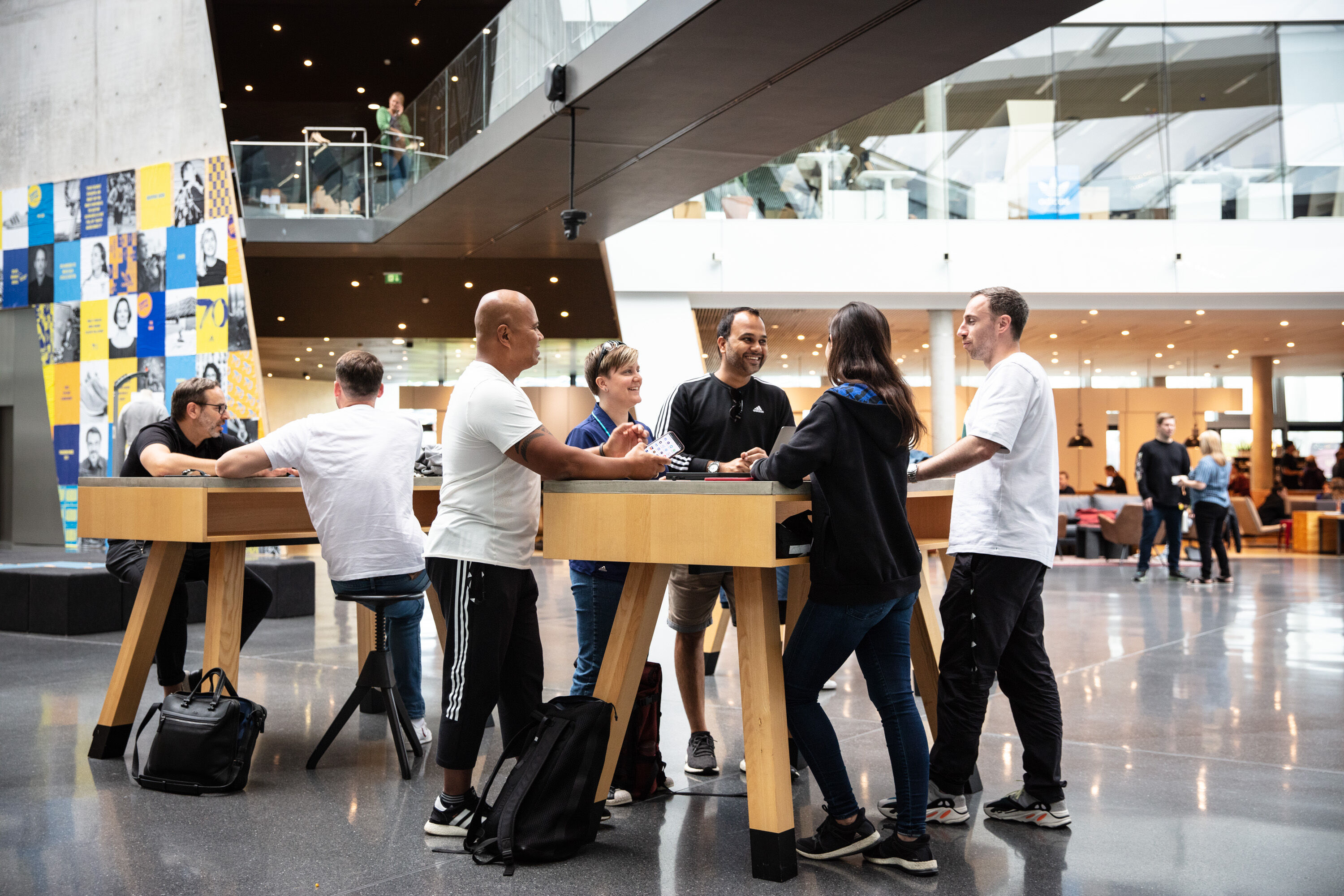 A group of people are gathered around a table in a modern building, appearing to be engaged in conversation and interaction.