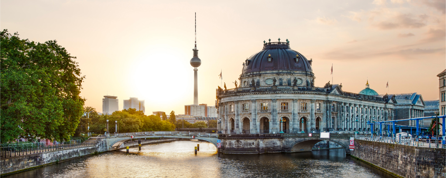 This is a panoramic view of the Spree River in Berlin, Germany, with the Bode Museum on the right and the Berlin TV Tower in the background during a beautiful sunset.