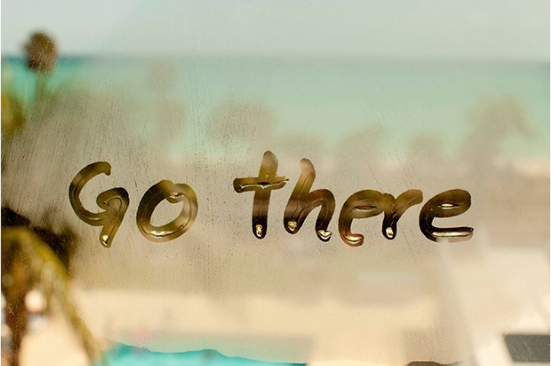 The image shows the words "Go there" written on a steamy surface, possibly a window, with a blurred background suggesting an outdoor scene.