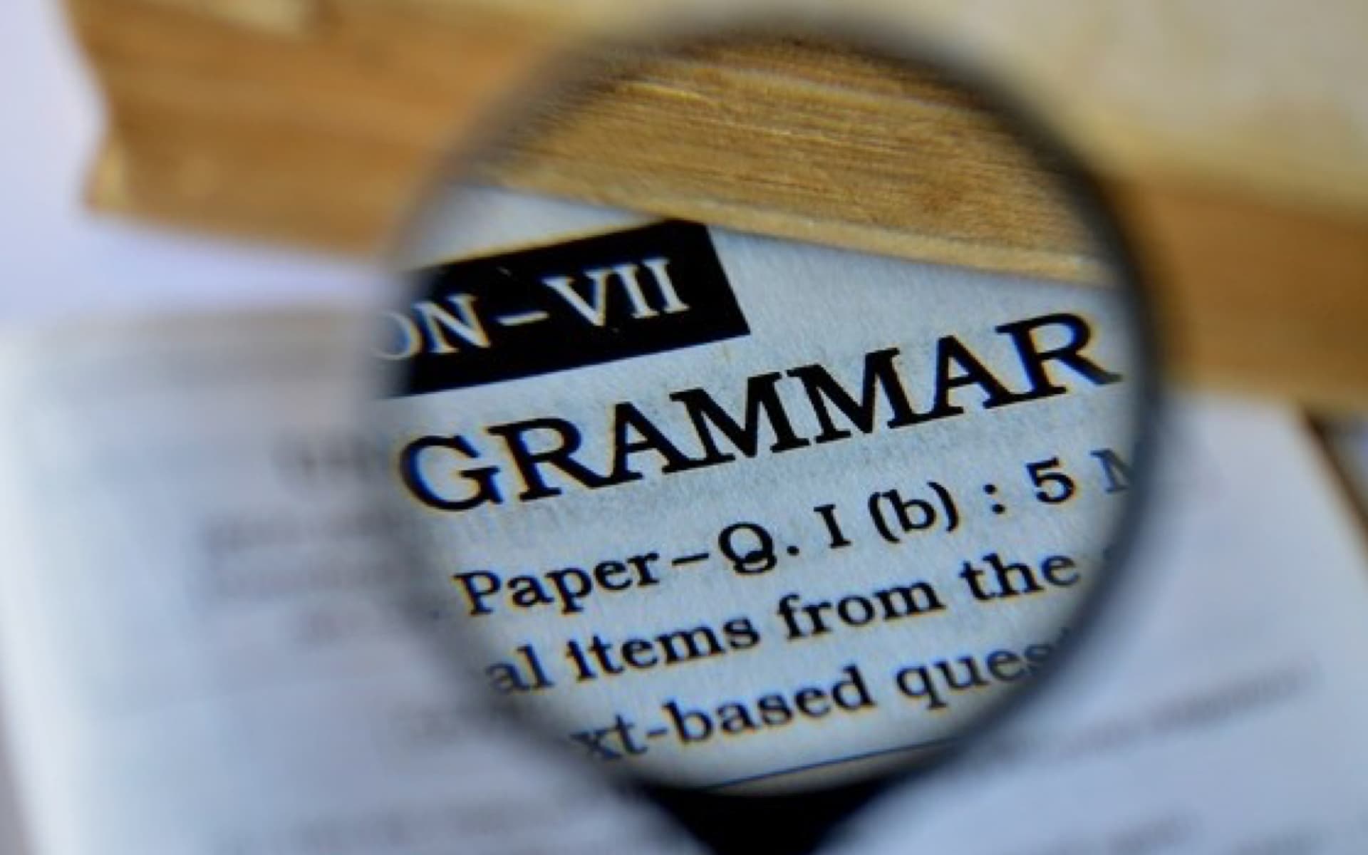 This image shows an open book with the word "GRAMMAR" magnified by a magnifying glass, highlighting the importance of grammar in language.
