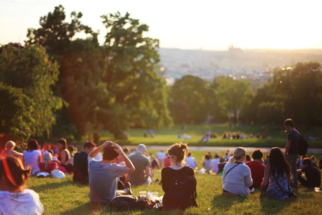 A group of people are enjoying a sunny day in the park, sitting on the grass and looking out at a city in the distance.