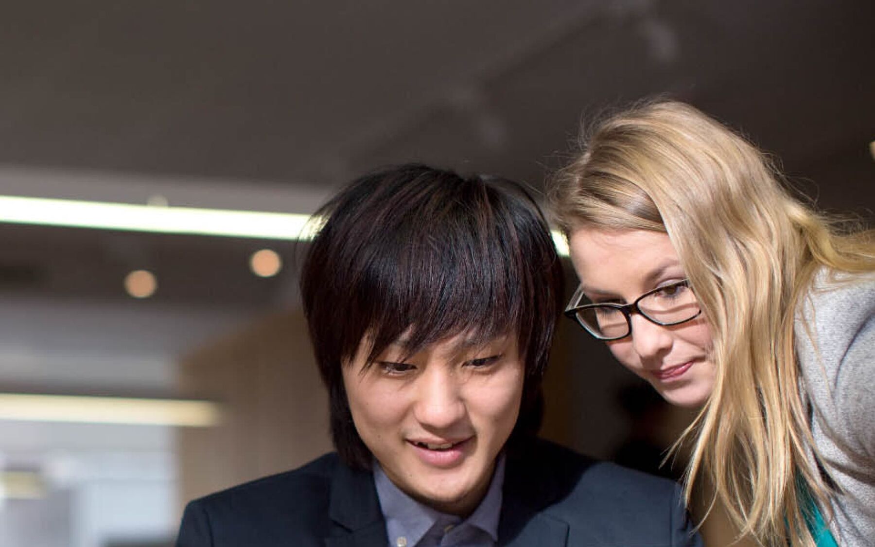 Two colleagues, one of East Asian descent and the other Caucasian, are intently focused on a screen, possibly collaborating on a project or reviewing information together.