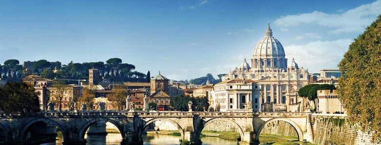 This is a panoramic view of Rome, Italy, featuring the Tiber River, Ponte Sant'Angelo bridge, and the magnificent St. Peter's Basilica in the background under a clear blue sky.