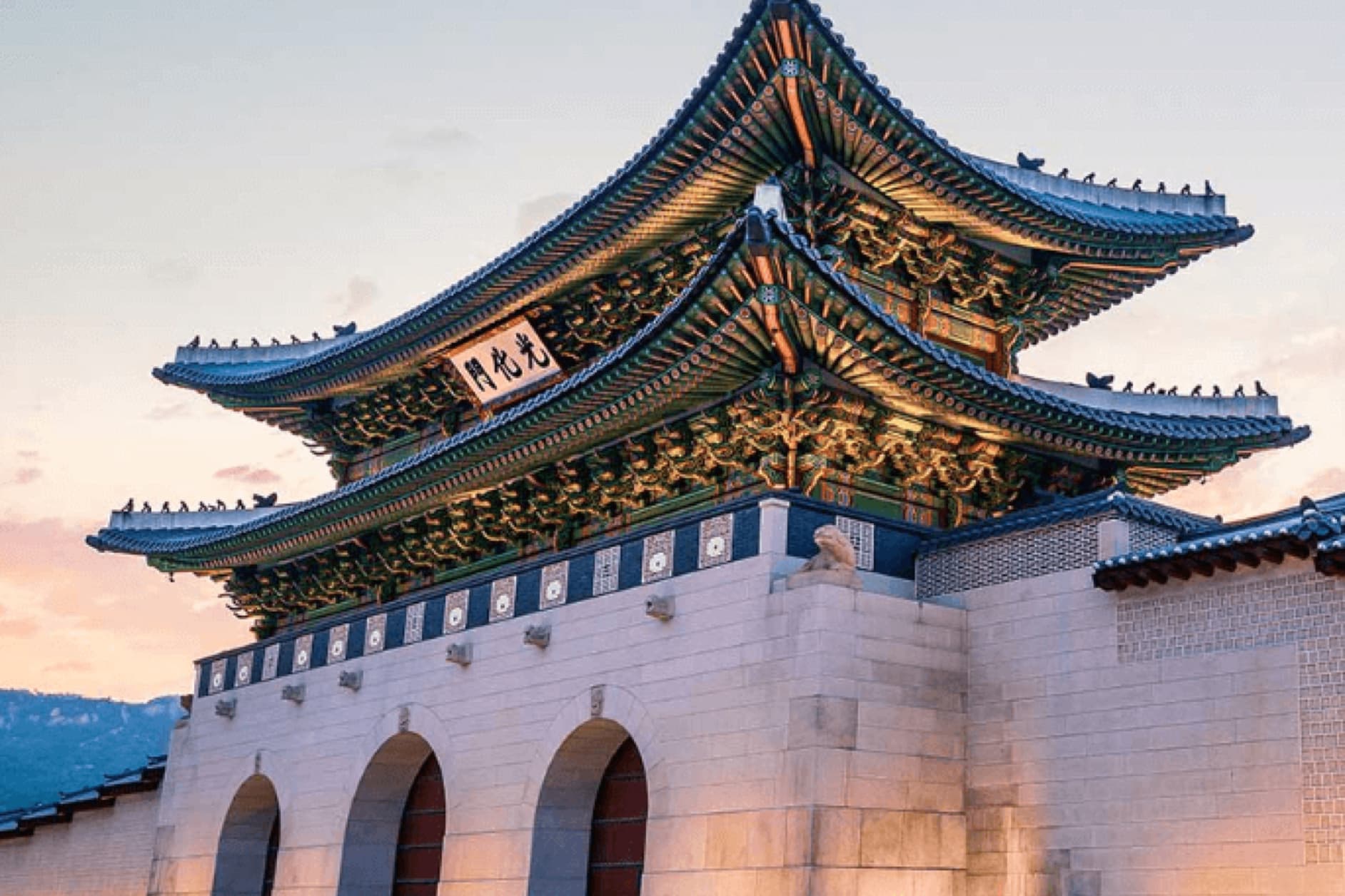 The image displays Gyeongbokgung Palace in Seoul, South Korea, showcasing its impressive architecture and traditional Korean design, illuminated by the soft light of sunset.