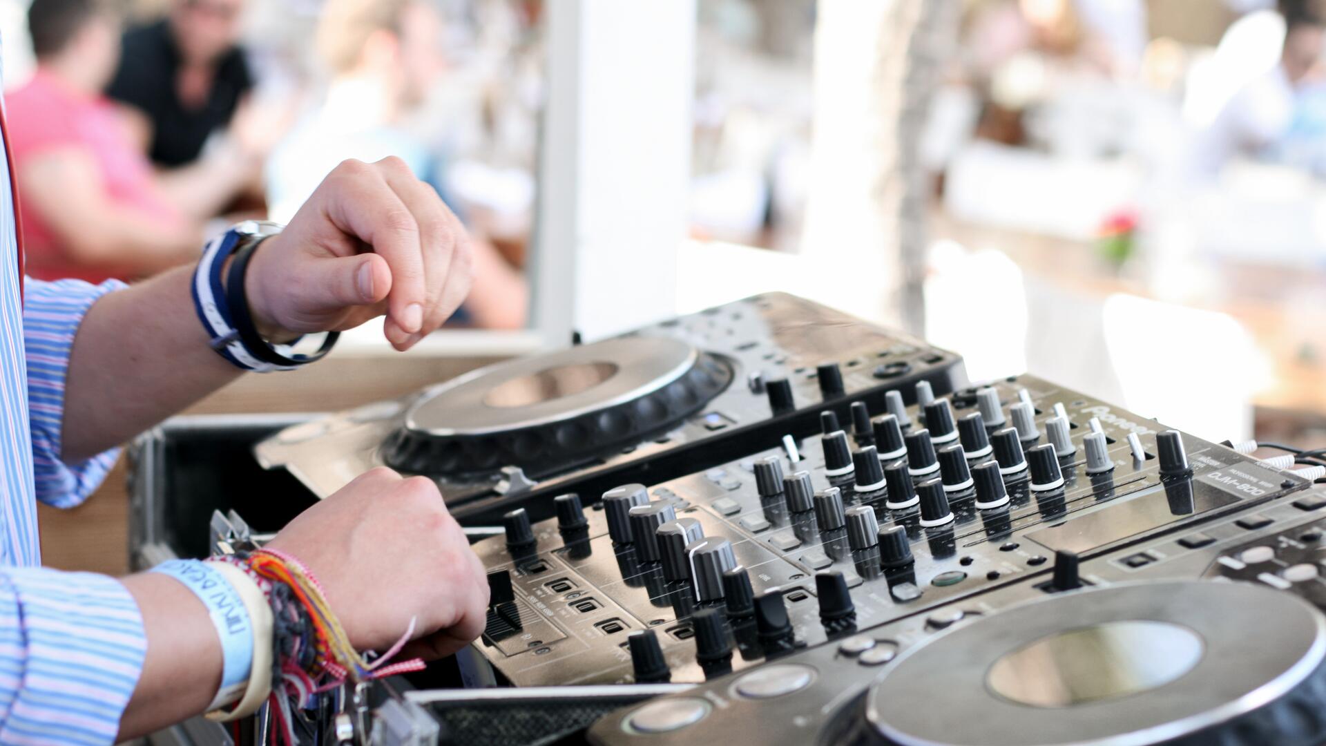 A DJ is mixing music using a DJ controller and two turntables while performing at an event.