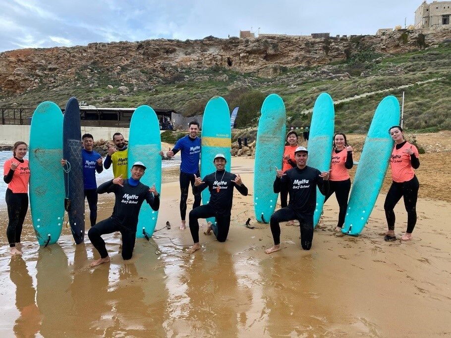 A group of surfers pose with their surfboards on the beach, ready for a lesson or a session.