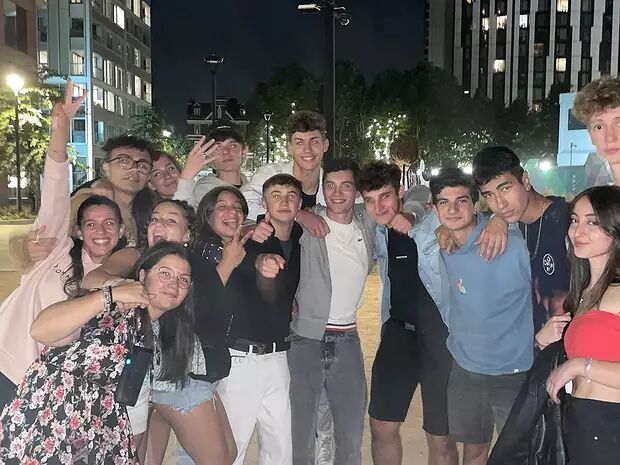 A group of young people pose for an outdoor photo at night, with some smiling and making peace signs.