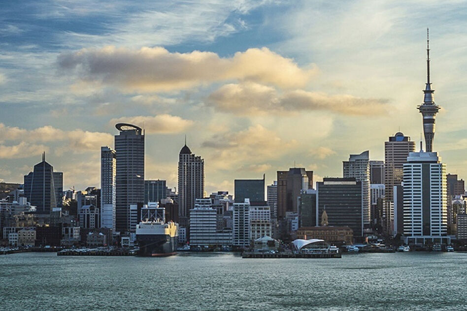 A panoramic view of the Auckland skyline during the day, featuring skyscrapers and the Sky Tower set against the water.