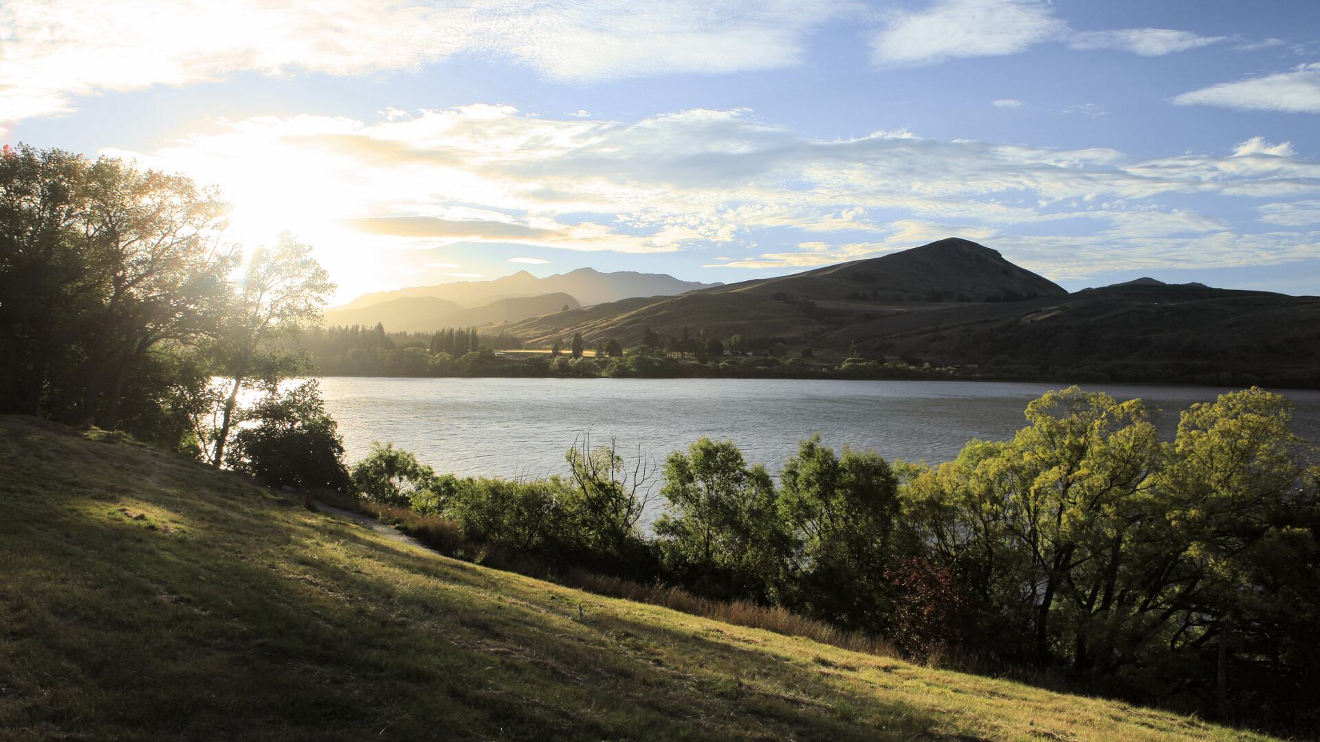 The image shows a serene lake at sunrise, with the sun