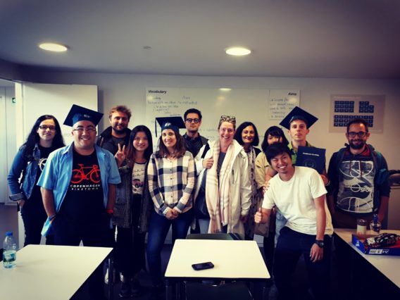A group of students wearing graduation caps pose for a photo in a classroom setting, with a whiteboard visible in the background.