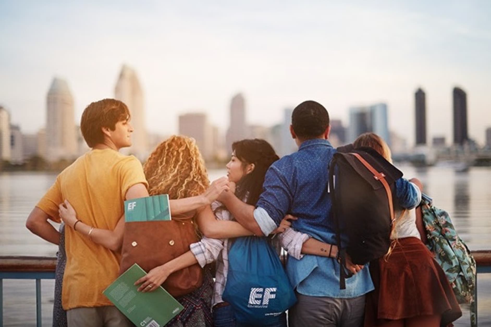 A group of young students with backpacks are enjoying a scenic view of a city skyline, likely on a school trip or exchange program.