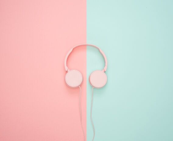 A pair of pastel pink headphones rests on a split background of pale pink and mint green paper, creating a minimalist and clean aesthetic.