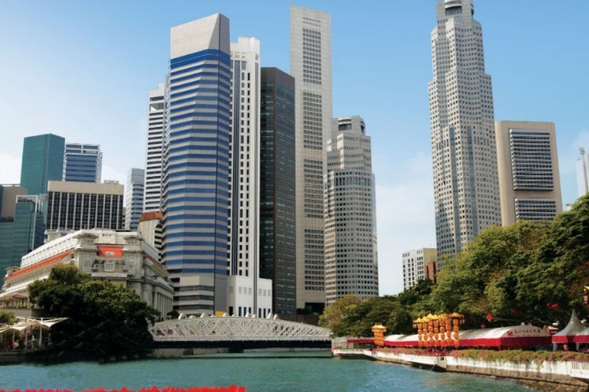 A modern cityscape featuring tall skyscrapers rising above a river under a clear blue sky. A bridge is visible in the foreground, complementing the skyline.